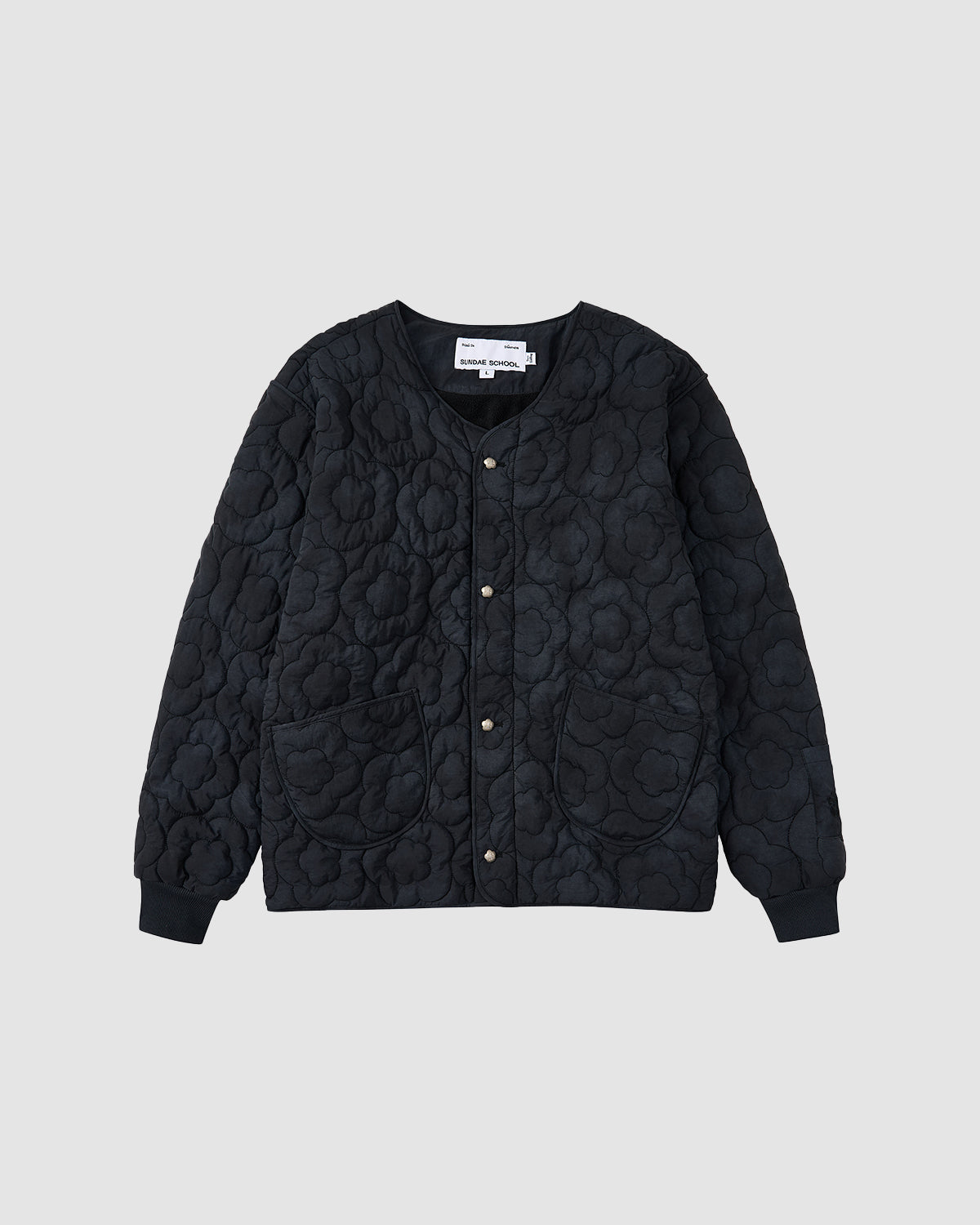 The BLACK MOCHI QUILTED MILITARY LINER by Sundae School features a round neckline, snap buttons, two large front pockets, and floral stitching—ideal for transitional weather. Shown in black on a light gray background.