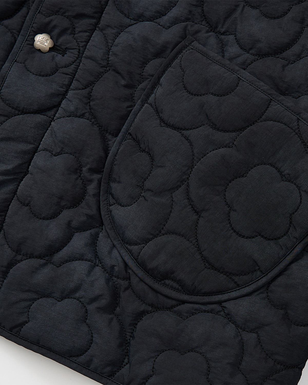 Close-up of Sundae School's BLACK MOCHI QUILTED MILITARY LINER, showing a rounded pocket with metal snap and flower-patterned stitching inspired by classic Korean military jackets.