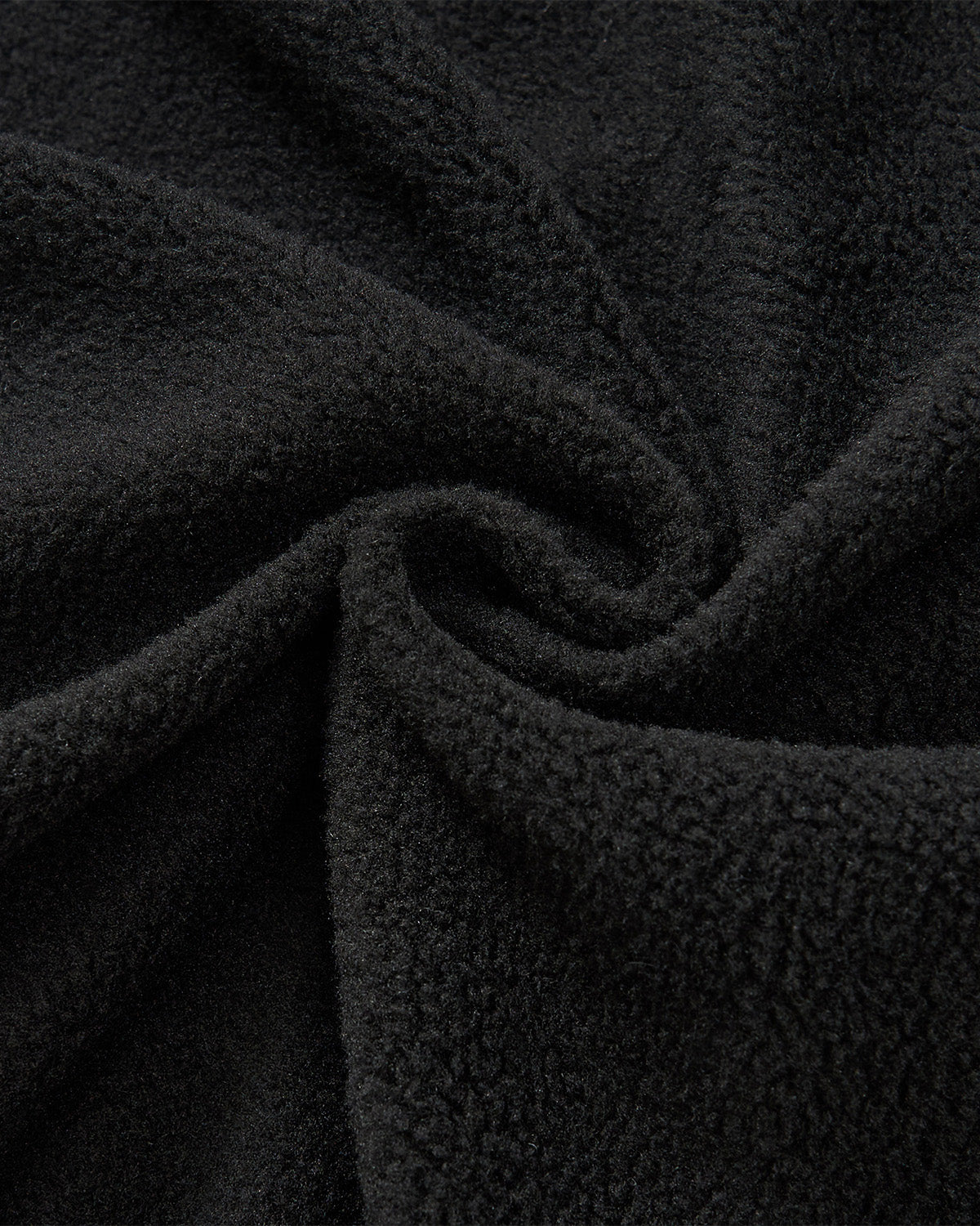 A close-up of plush, black fleece fabric with a textured, fuzzy surface and spiral folds—ideal as the cozy lining for Sundae School’s BLACK MOCHI QUILTED MILITARY LINER, perfect for transitional weather jackets.