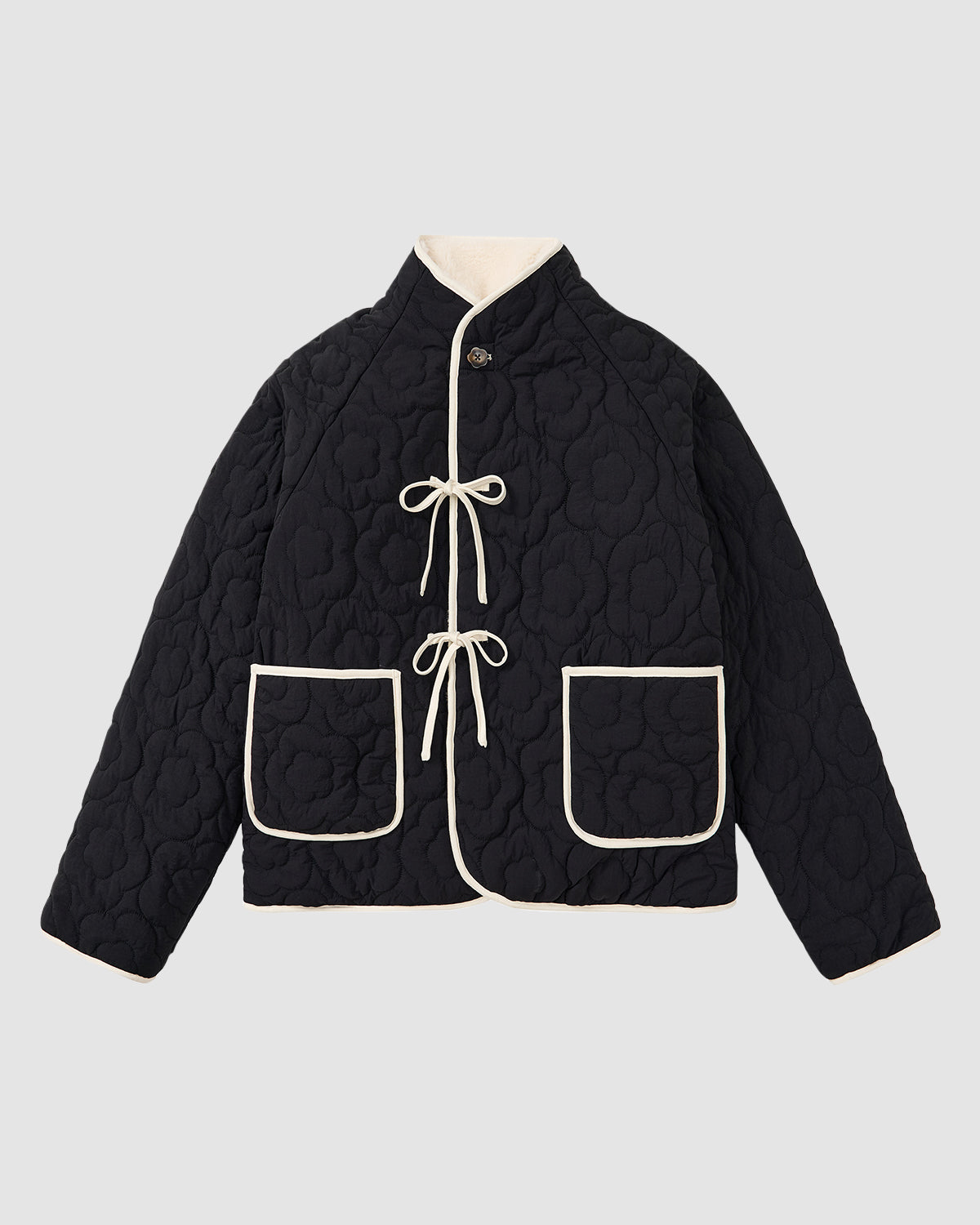 The BLACK IVORY REVERSIBLE FLOWER QUILTED JEOGORI FLEECE by Sundae School is a black Korean hanbok jacket with cream trim, high collar, long sleeves, floral quilted pattern, two front pockets and ties, offering a stylish reversible design.