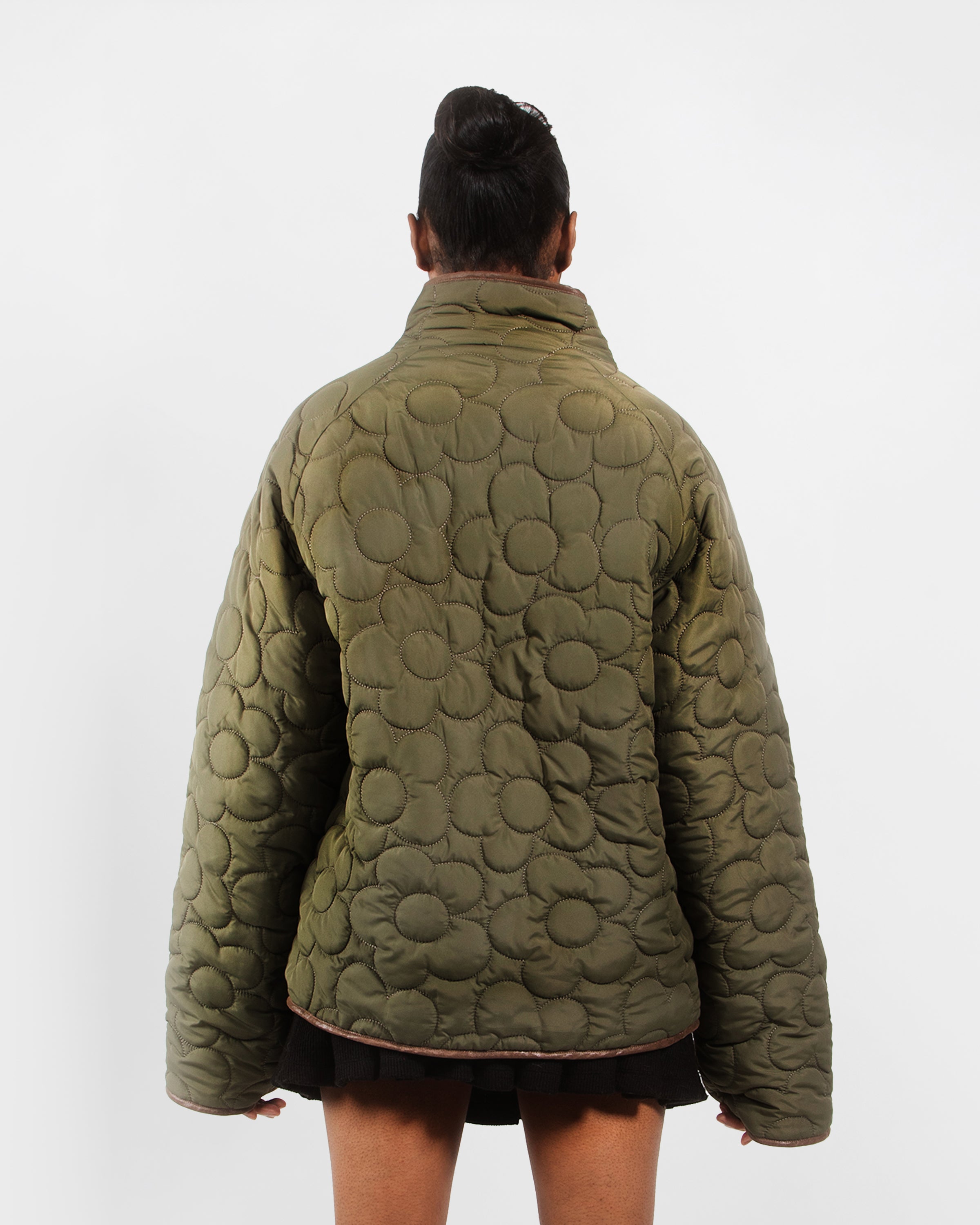 A person stands with their back to the camera in a Sundae School REVERSIBLE FLOWER QUILTED JEOGORI FLEECE—an oversized, olive green Korean hanbok jacket with circular stitching—paired with black shorts, set against a plain white background.