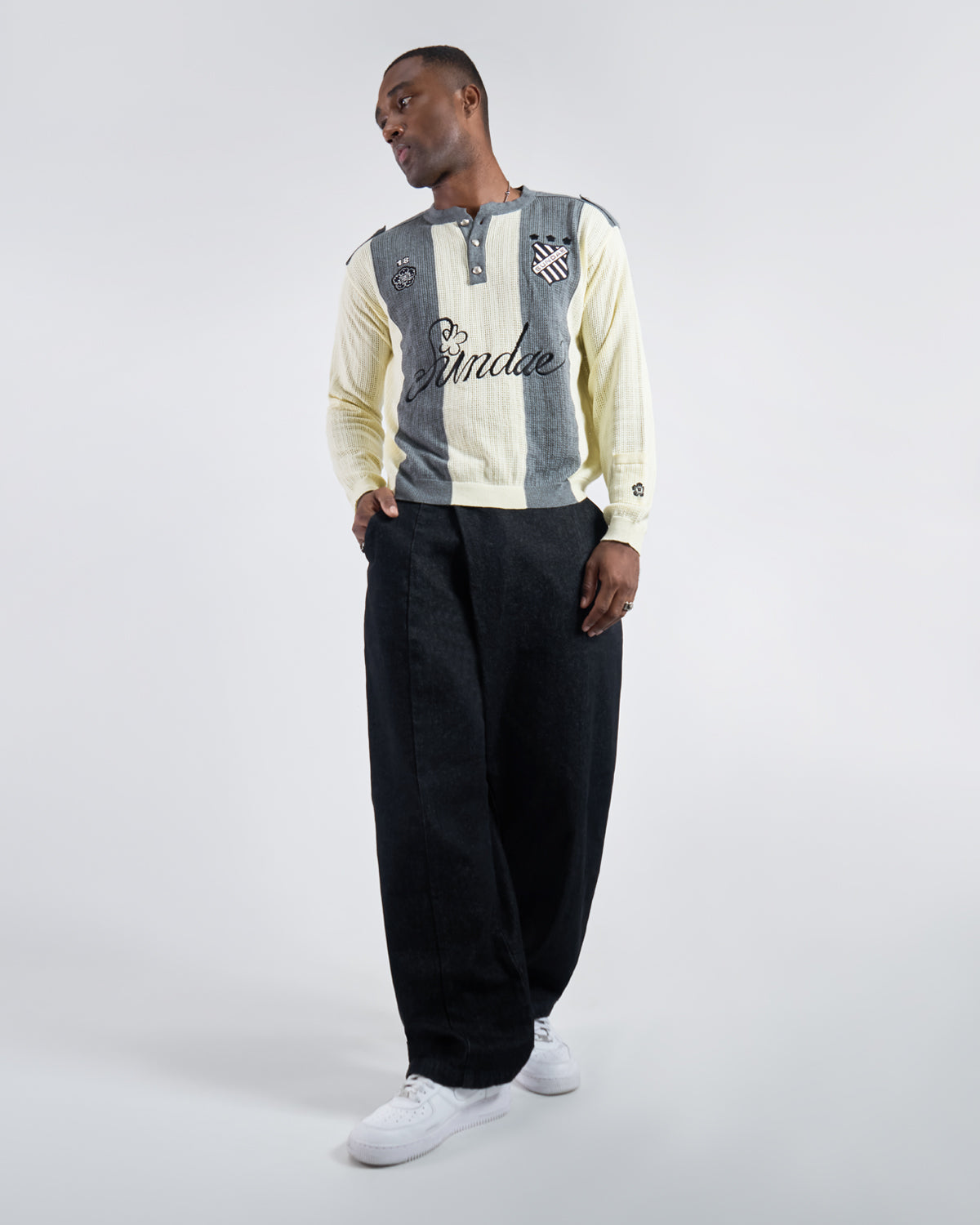 Full body side angle view of Butter Yellow Charcoal Sundae Soccer Jersey Knit styled with black wide-leg pants and white sneakers, demonstrating garment silhouette, fit, and movement in a relaxed standing pose against light background.