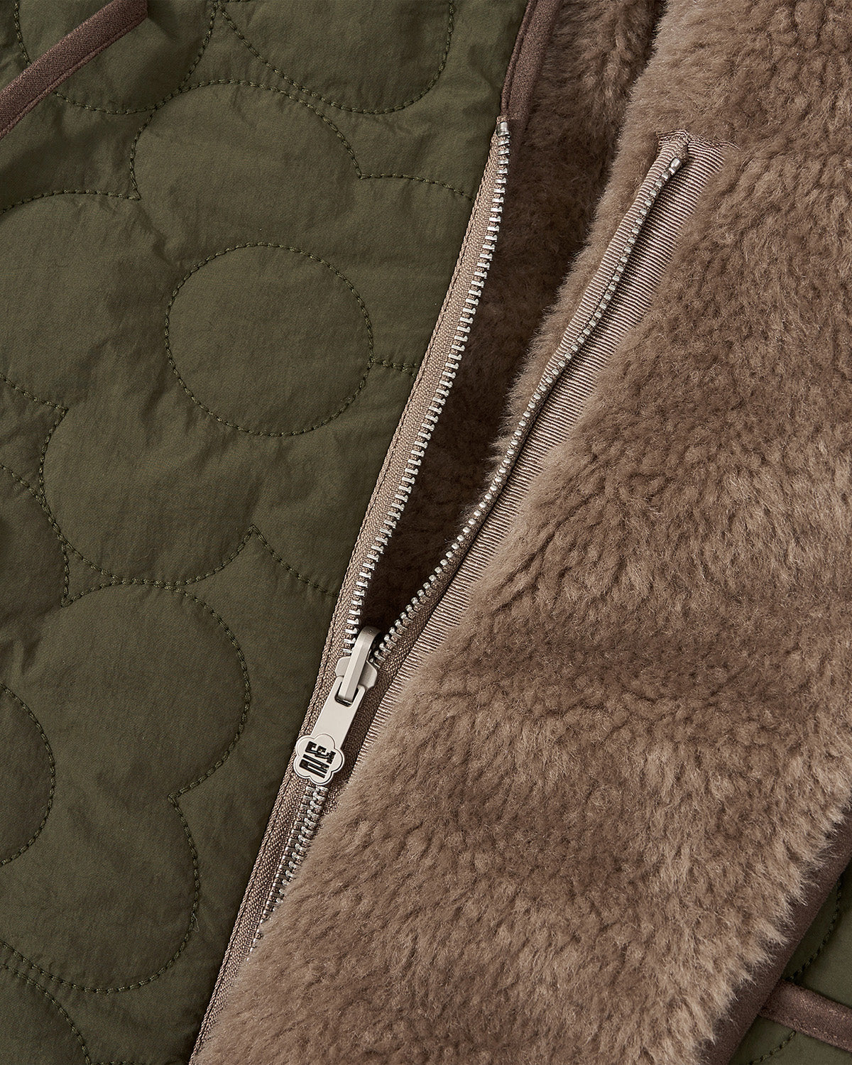 Close-up of Sundae School's REVERSIBLE FLOWER QUILTED JEOGORI FLEECE, showing khaki green floral quilting inspired by Korean hanbok jackets beside brown faux shearling, divided by a partially unzipped beige zipper.