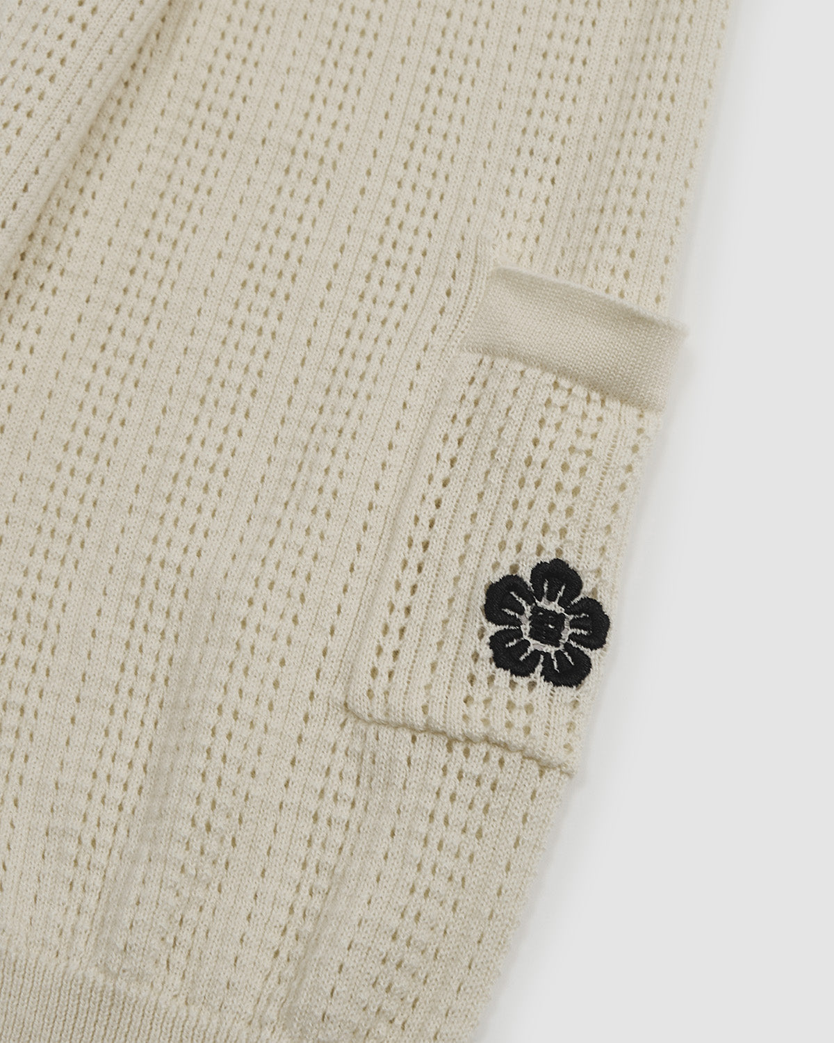 Close-up of Butter Yellow Charcoal Sundae Soccer Jersey Knit cream sleeve section showing small black hibiscus flower embroidered detail on ribbed knit texture, demonstrating subtle embroidered branding elements.