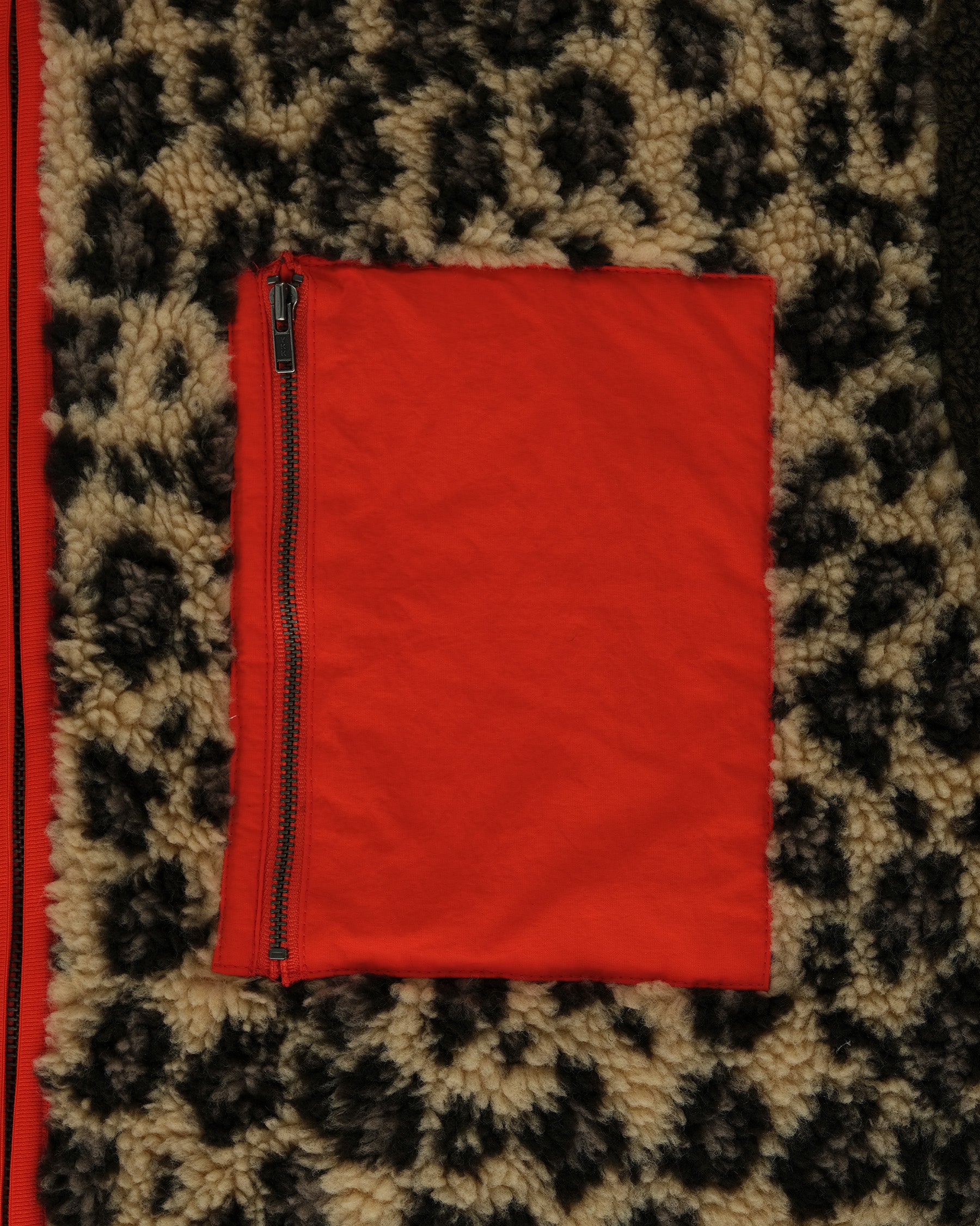A red zippered pocket sits on beige and dark brown leopard-print fleece, evoking the cozy style of Sundae School's Tiger Mom Fleece.
