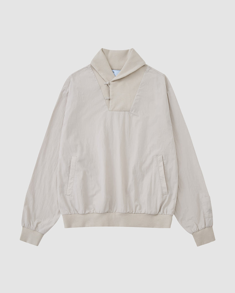 The IVORY SHAWL COLLAR ANORAK by Sundae School features long sleeves, a high collar, button details, front pockets, and elastic cuffs and hem. Made from a cotton-nylon shell in light beige and shown on a plain white background.