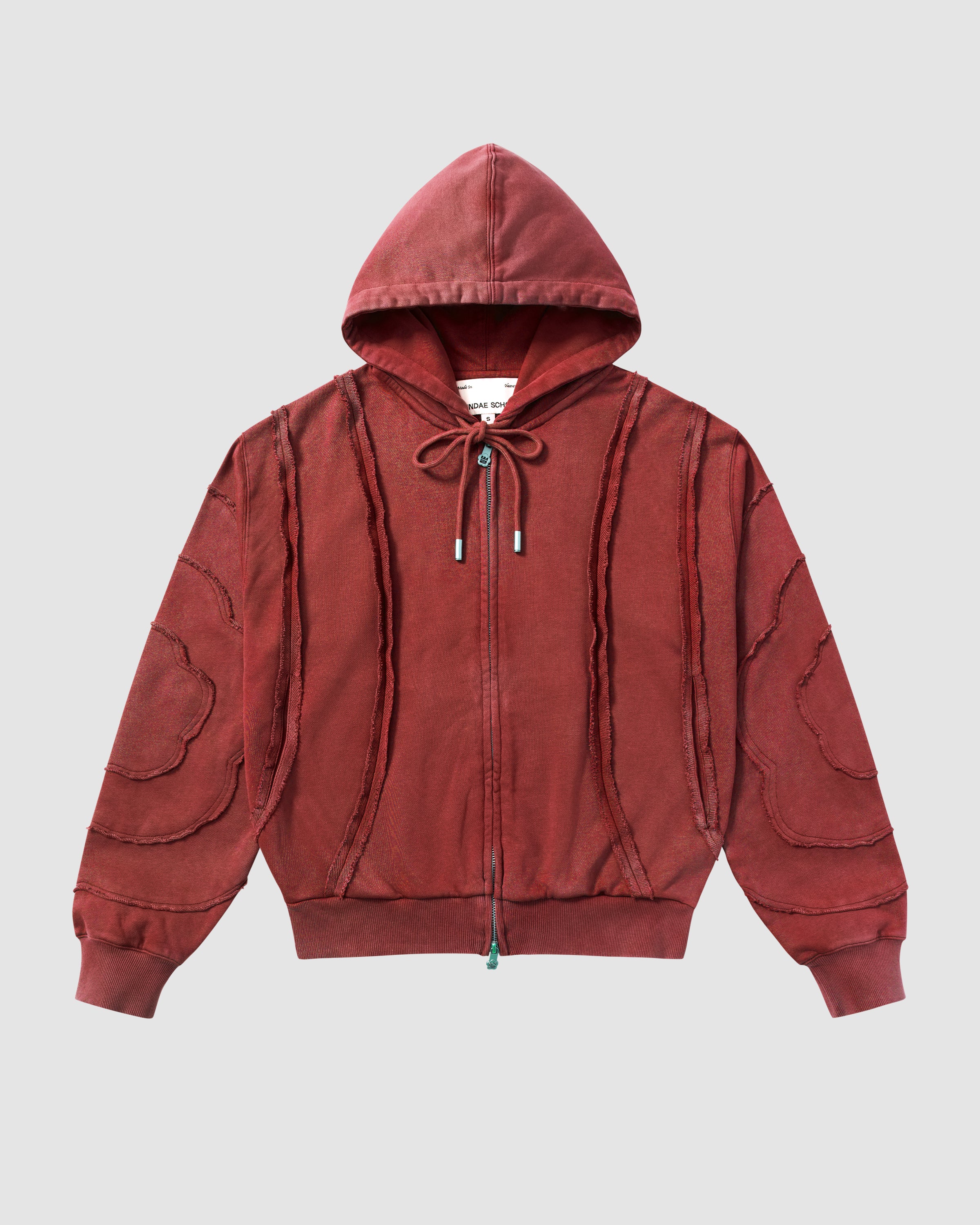 Red Mochi Haze Paneled Hoodie featuring garment washed red cotton with exposed curved seam details throughout body and sleeves, zip-up construction with drawstring hood, ribbed cuffs and hem, relaxed oversized fit silhouette, flat lay product shot on light background.