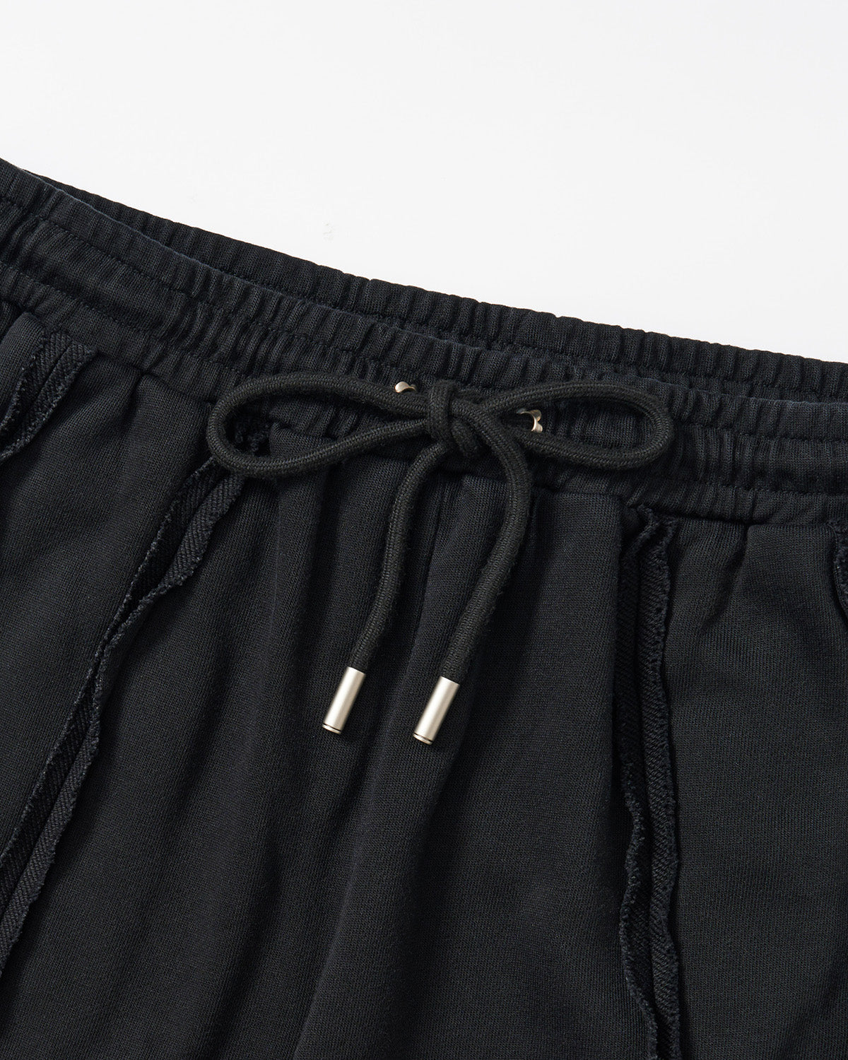 Black Mochi Haze Paneled Sweatpants waistband detail showing elastic band with drawstring ties and metal aglets, exposed seam construction visible, garment washed black cotton texture, flat lay on light background.