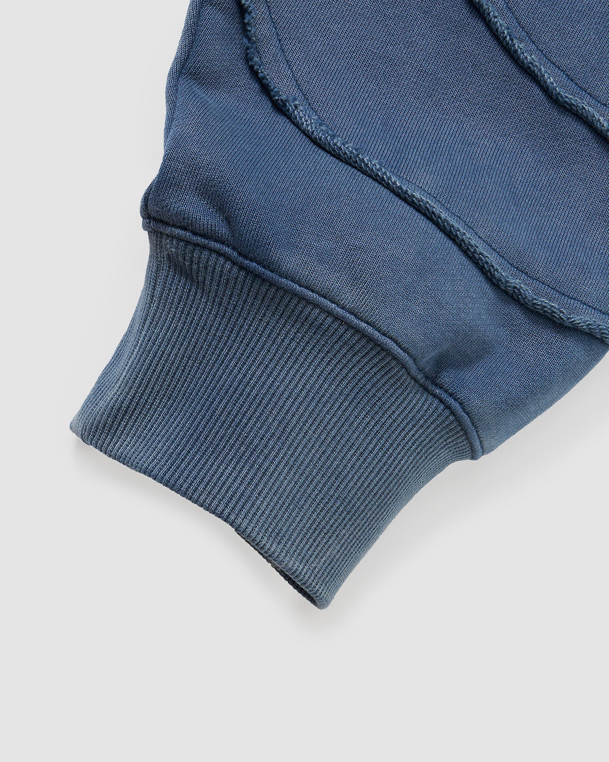 Indigo Mochi Haze Paneled Hoodie featuring garment washed indigo cotton with exposed curved seam details paired with matching indigo Mochi Haze Paneled Sweatpants showing back construction details, relaxed oversized fit silhouette, modeled on light background, shown in back view.