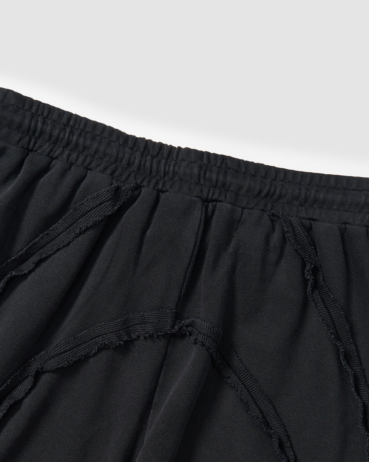 Black Mochi Haze Paneled Sweatpants close-up detail showing curved exposed seam construction with frayed edges and elastic waistband, garment washed black cotton fabric texture.