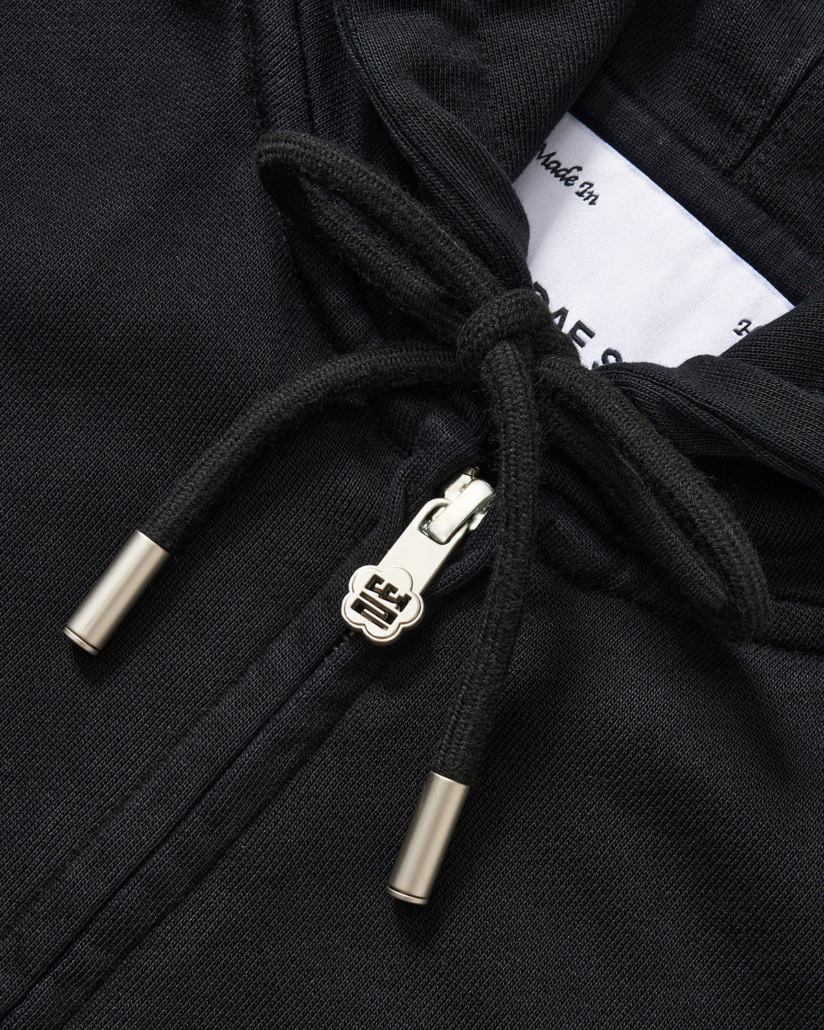 Black Mochi Haze Paneled Hoodie close-up detail shot showing drawstring hood with metal hardware, zip closure with branded zipper pull, brand label visible, and exposed seam details on garment washed black cotton.