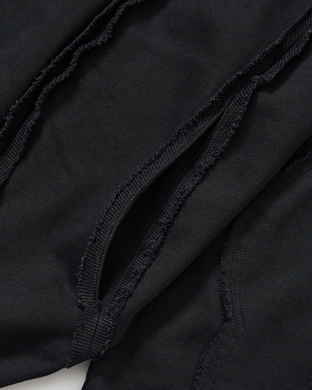Black Mochi Haze Paneled Hoodie close-up detail shot showing curved exposed seam construction with frayed edges and distressed finishing on garment washed black cotton fabric.