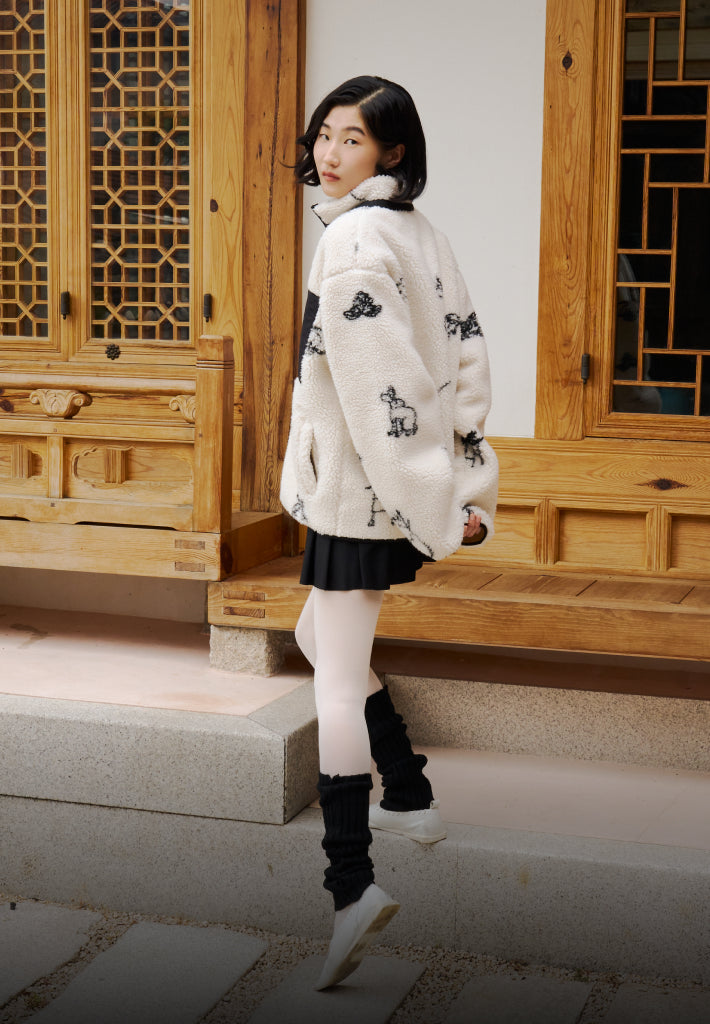 A girl wearing Sundae School Kiwa Fleece standing in front of Korean traditional house hanok with one of her leg on the step and the other leg on the floor.