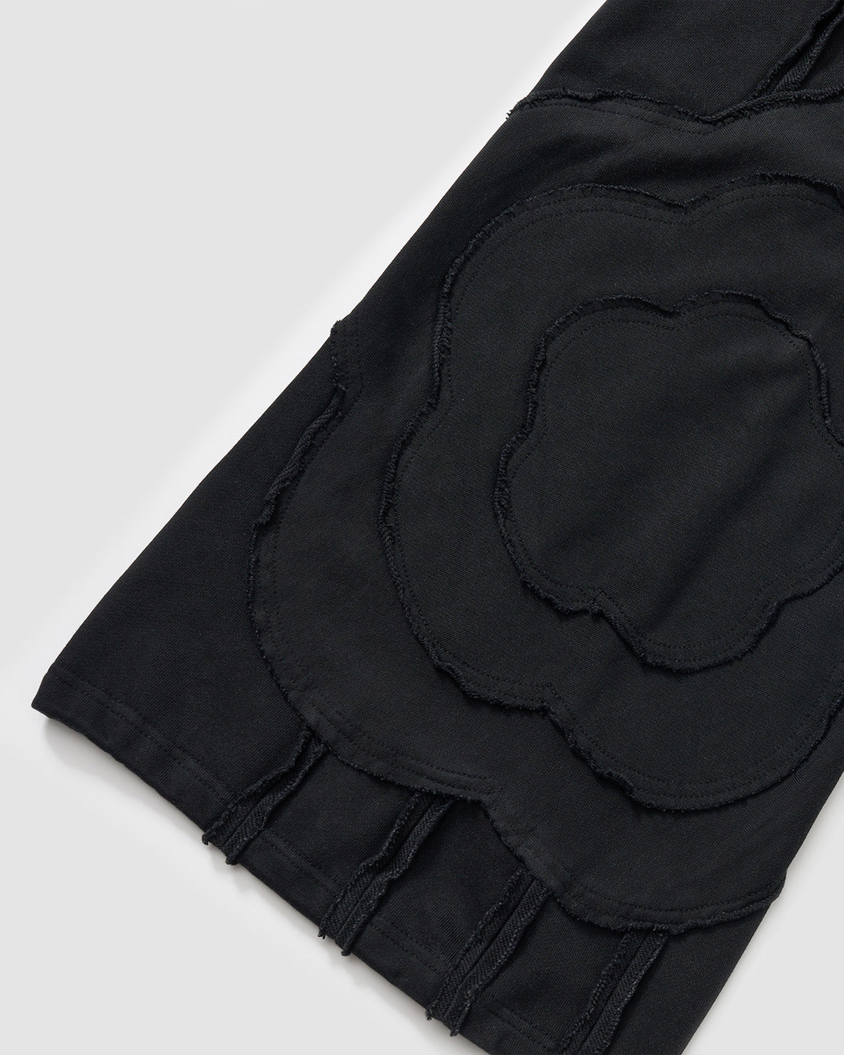 Black Mochi Haze Paneled Sweatpants close-up detail showing large curved exposed seam construction with flower-like pattern and frayed edges on garment washed black cotton fabric.