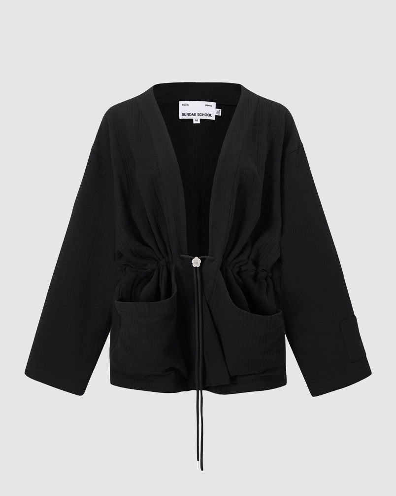Sundae School Quilted Bolo Tie Cardigan in black quilted cotton featuring silver metal bolo tie with '떨' logo, deep front pockets, and relaxed fit silhouette on light background