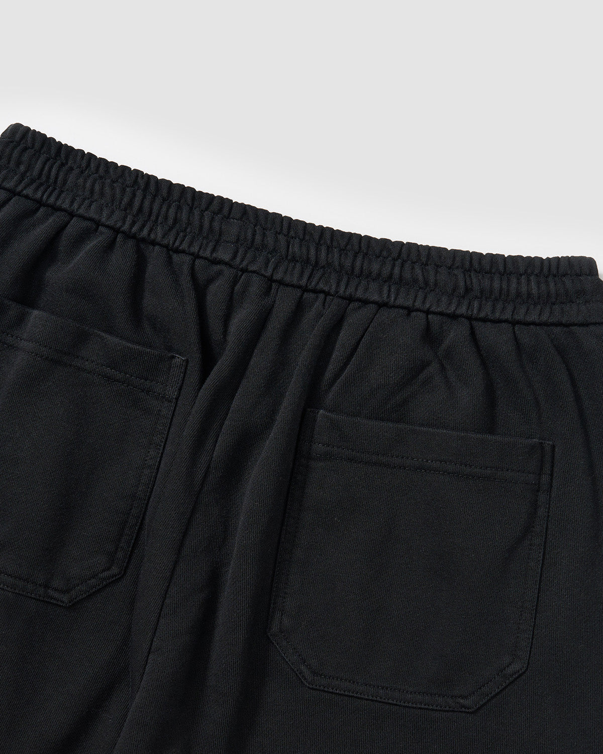 Black Fade Black Snap Sweatpants back waistband detail showing elastic band and back pockets, vintage fade washed black cotton texture, flat lay on light background.