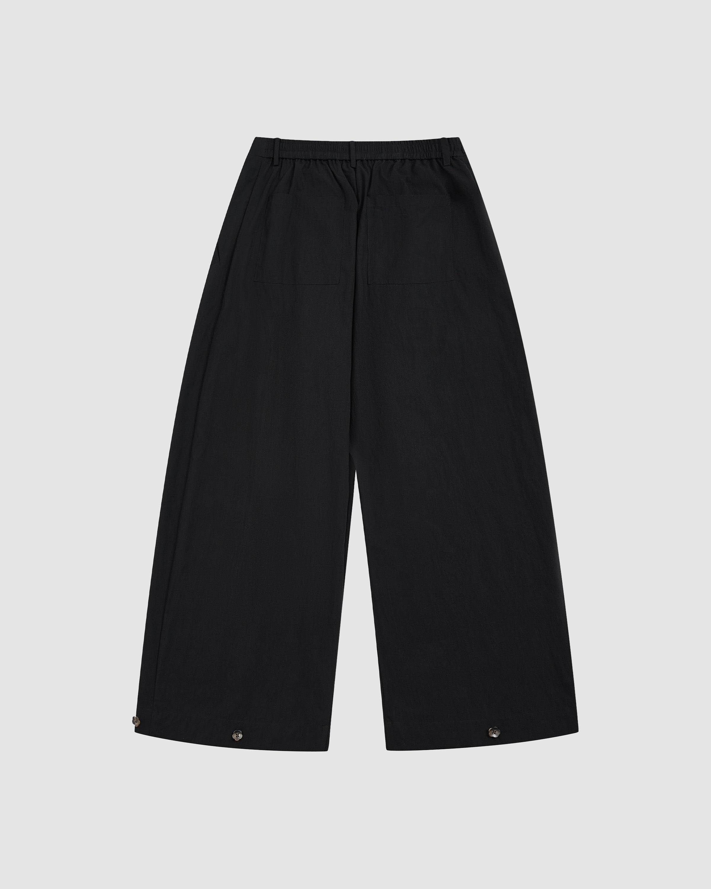 Sundae School Black Pleated Nylon Pants back view showing wide-leg silhouette with hem button details and elastic waistband on light background