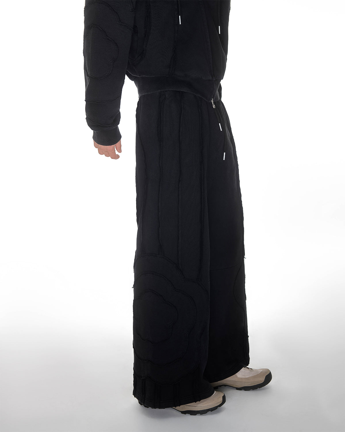 Black Mochi Haze Paneled Sweatpants full leg detail showing exposed curved seam construction throughout length, relaxed wide-leg fit with distressed finishing, garment washed black cotton fabric, photographed on light background.