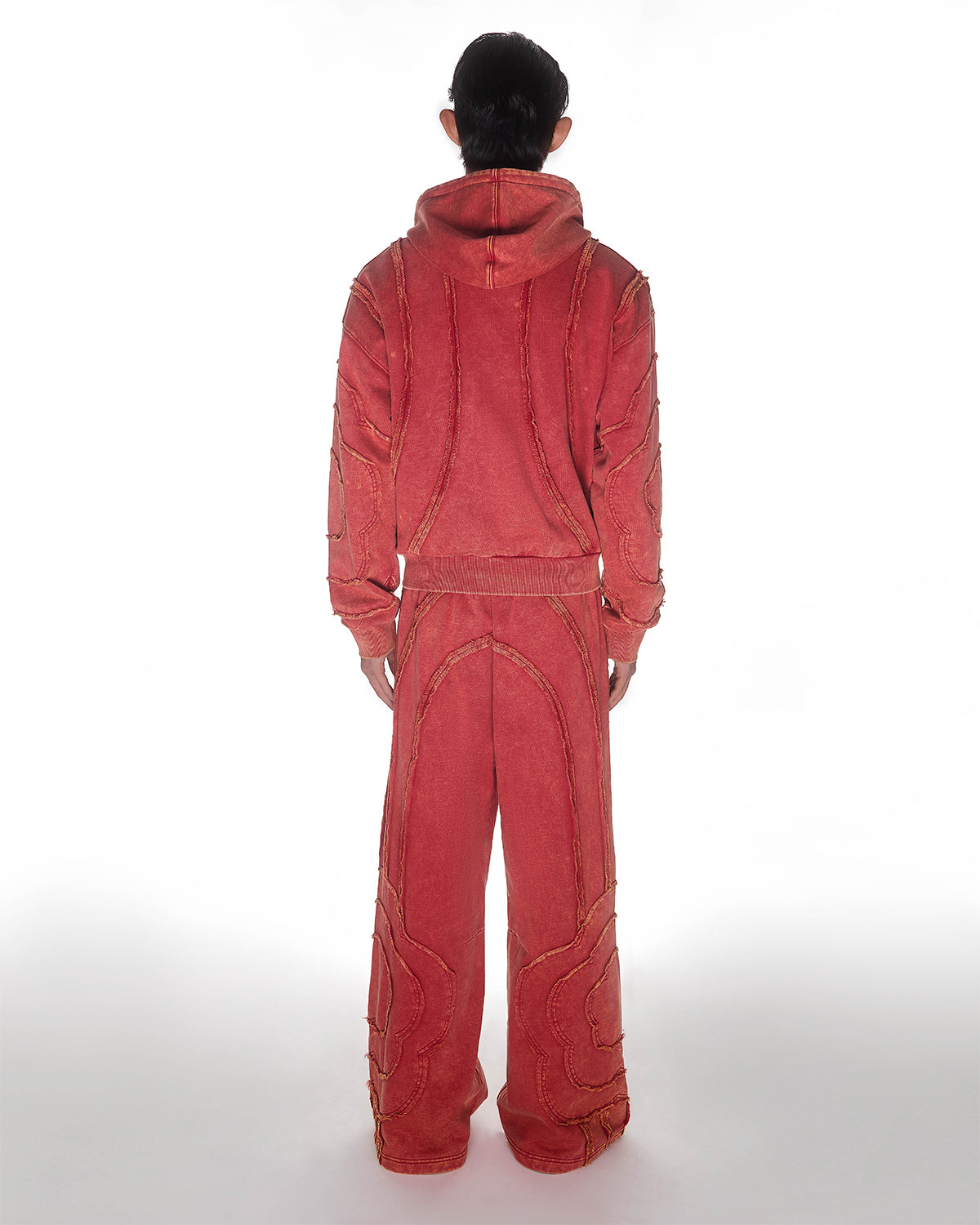 Red Mochi Haze Paneled Hoodie featuring washed red cotton with exposed curved seam details, paired with matching red sweatpants showing back construction details, relaxed oversized fit silhouette, modeled on light background, shown in back view.