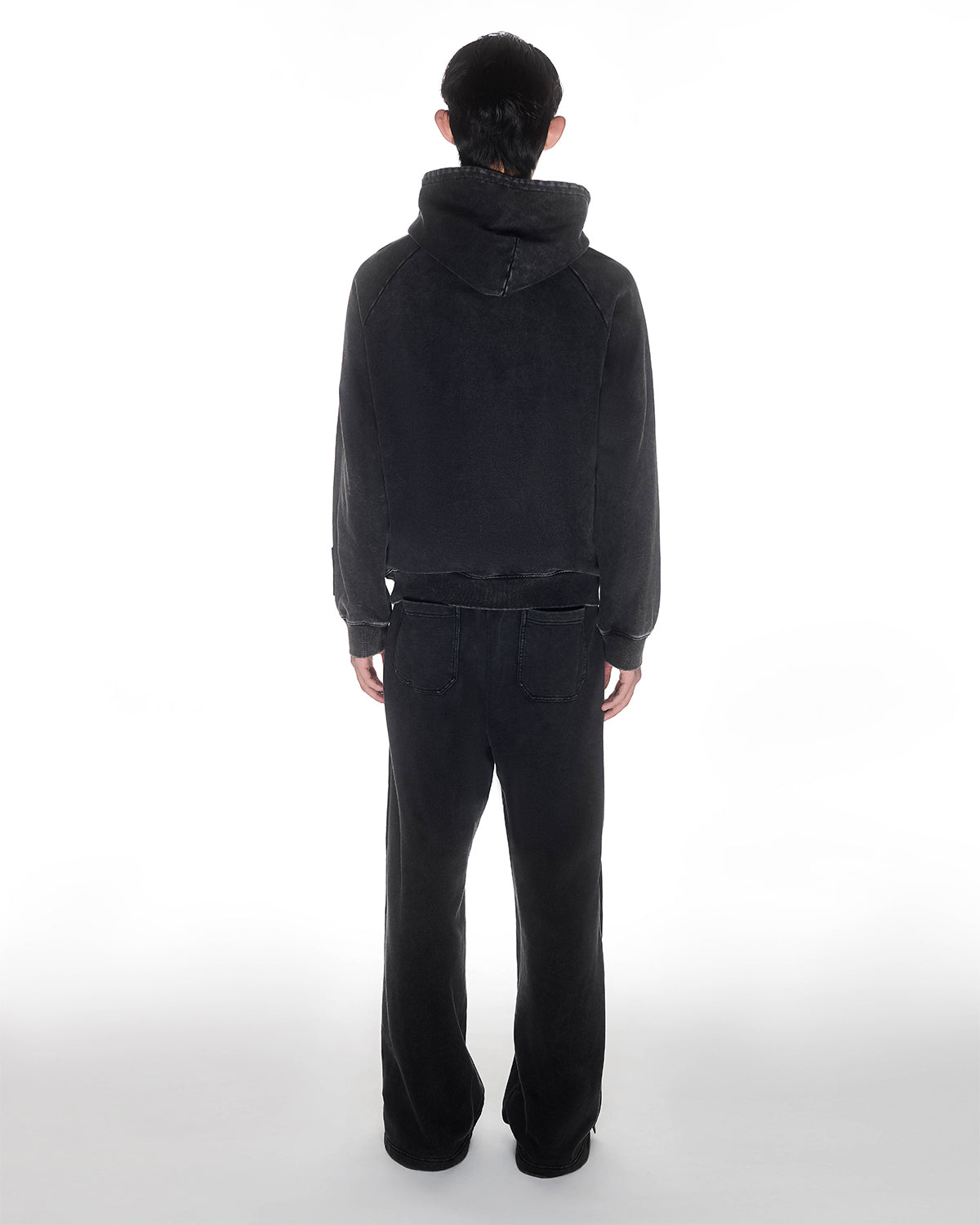 Black garment washed cotton Fade Black Hanbok Hoodie with custom dome snap details on hood paired with matching black Fade Black Snap Sweatpants showing back construction details, relaxed oversized fit silhouette, modeled on light background, shown in back view.
