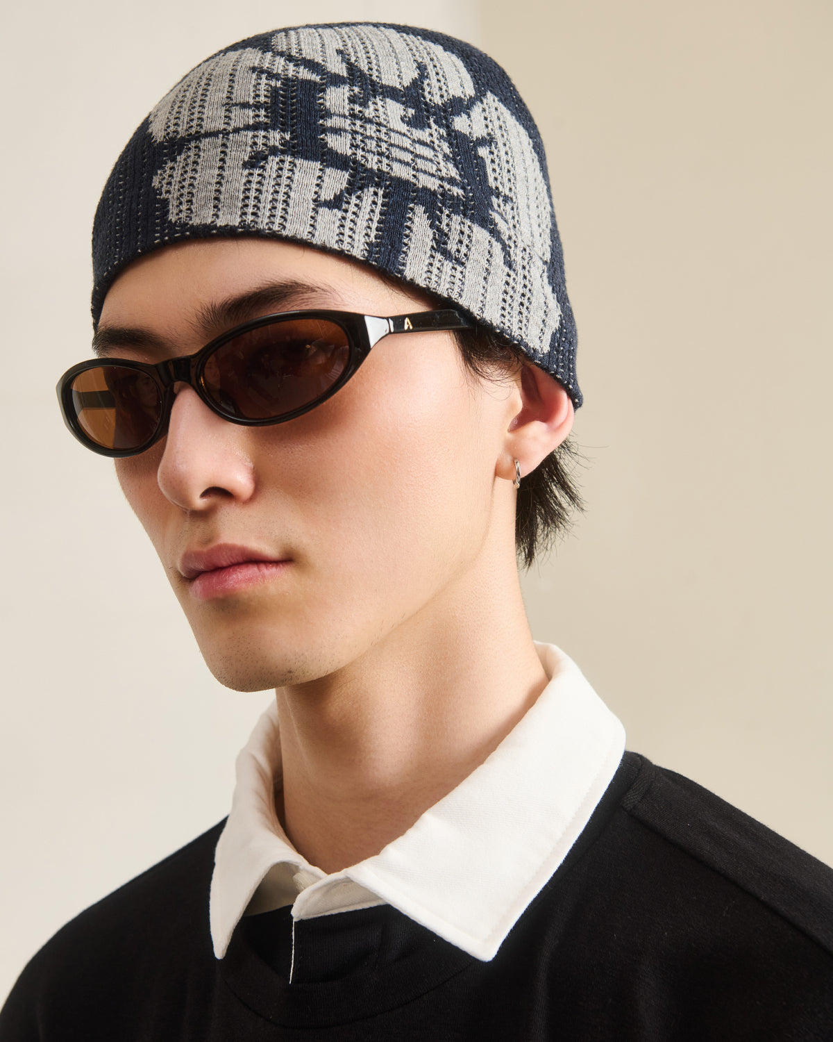 A young person in dark sunglasses, a black shirt with a white collar, and the NAVY DDUL KNIT BEANIE by Sundae School poses against a neutral background.