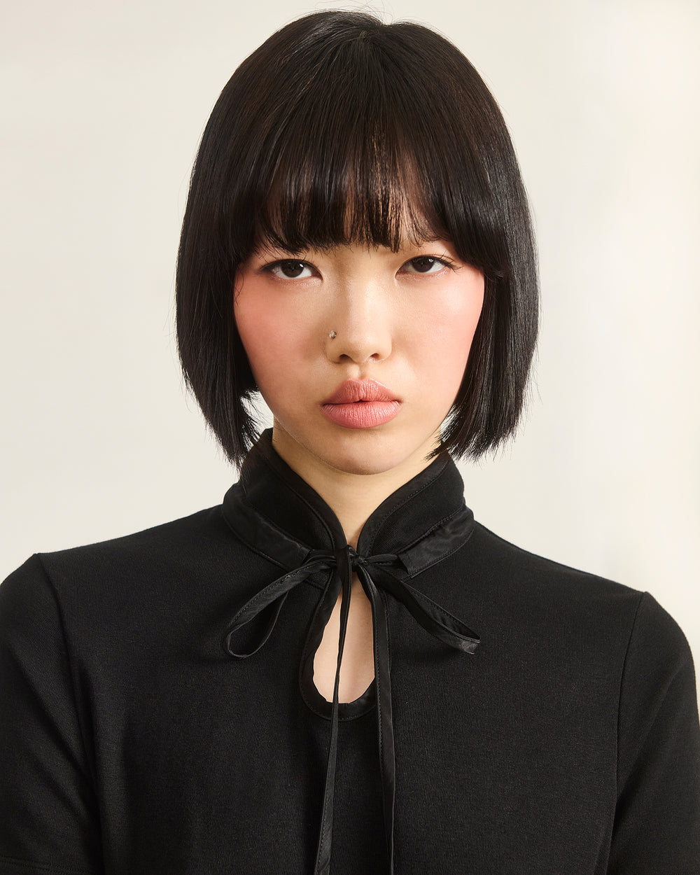 A person with straight black bobbed hair and bangs wears the Sundae School BLACK RIBBON TIE POLO, looking directly at the camera with a neutral expression against a light background.