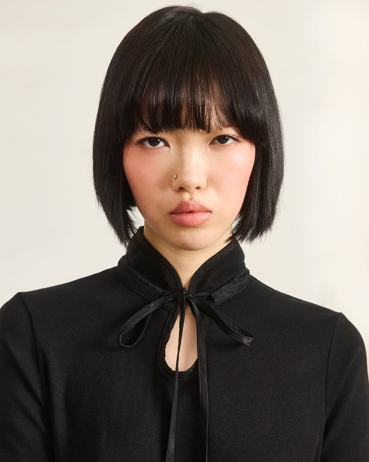 A person with straight black bobbed hair and bangs wears the Sundae School BLACK RIBBON TIE POLO, looking directly at the camera with a neutral expression against a light background.