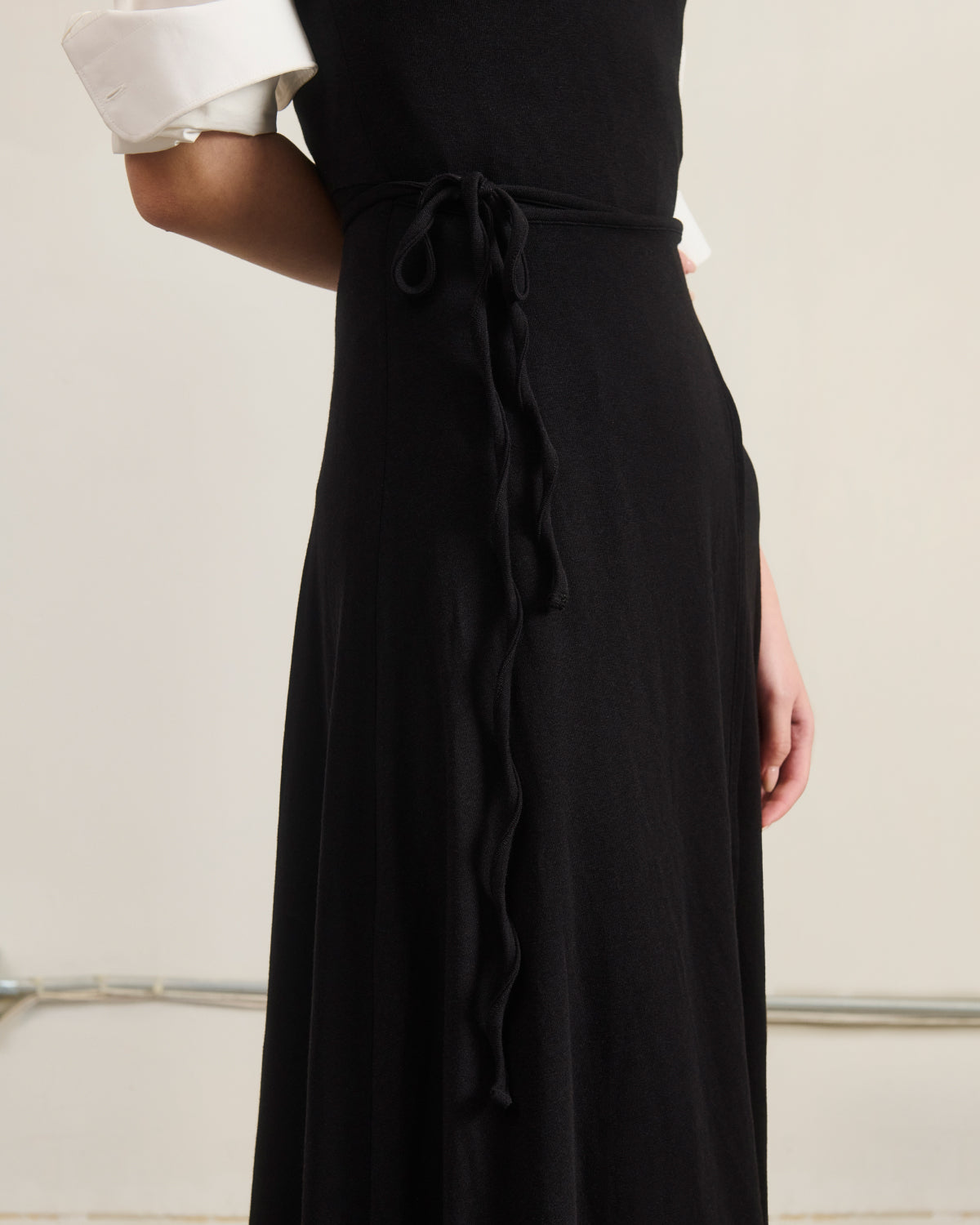 A person wearing the Sundae School BLACK CINDY POLO DRESS, styled over a white rolled-sleeve shirt and featuring a thin waist tie, is shown from the torso up against a plain background.