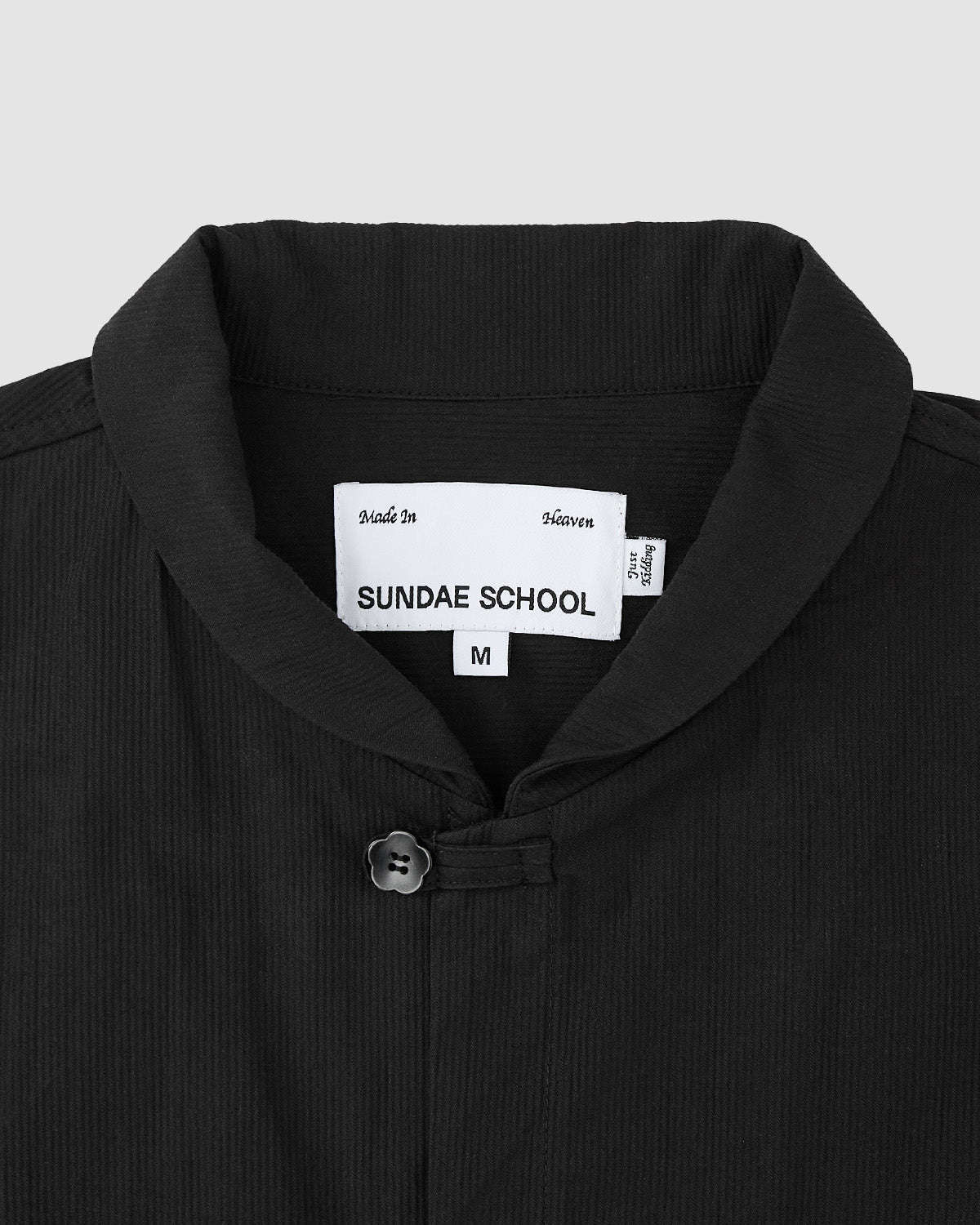 Close-up of the BLACK CHINA COLLAR KNOT SHACKET by Sundae School, featuring a black collar with a single button at the neckline. The inside label reads Sundae School, with tags for 