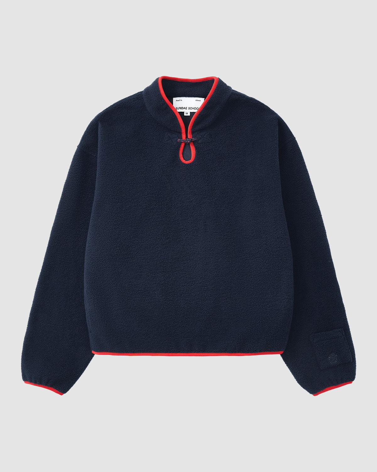 The NAVY TEARDROP KNOT FLEECE by Sundae School features a cozy navy fleece with long sleeves, a high collar, front half-zip with red trim, and red accents on the cuffs and hem.