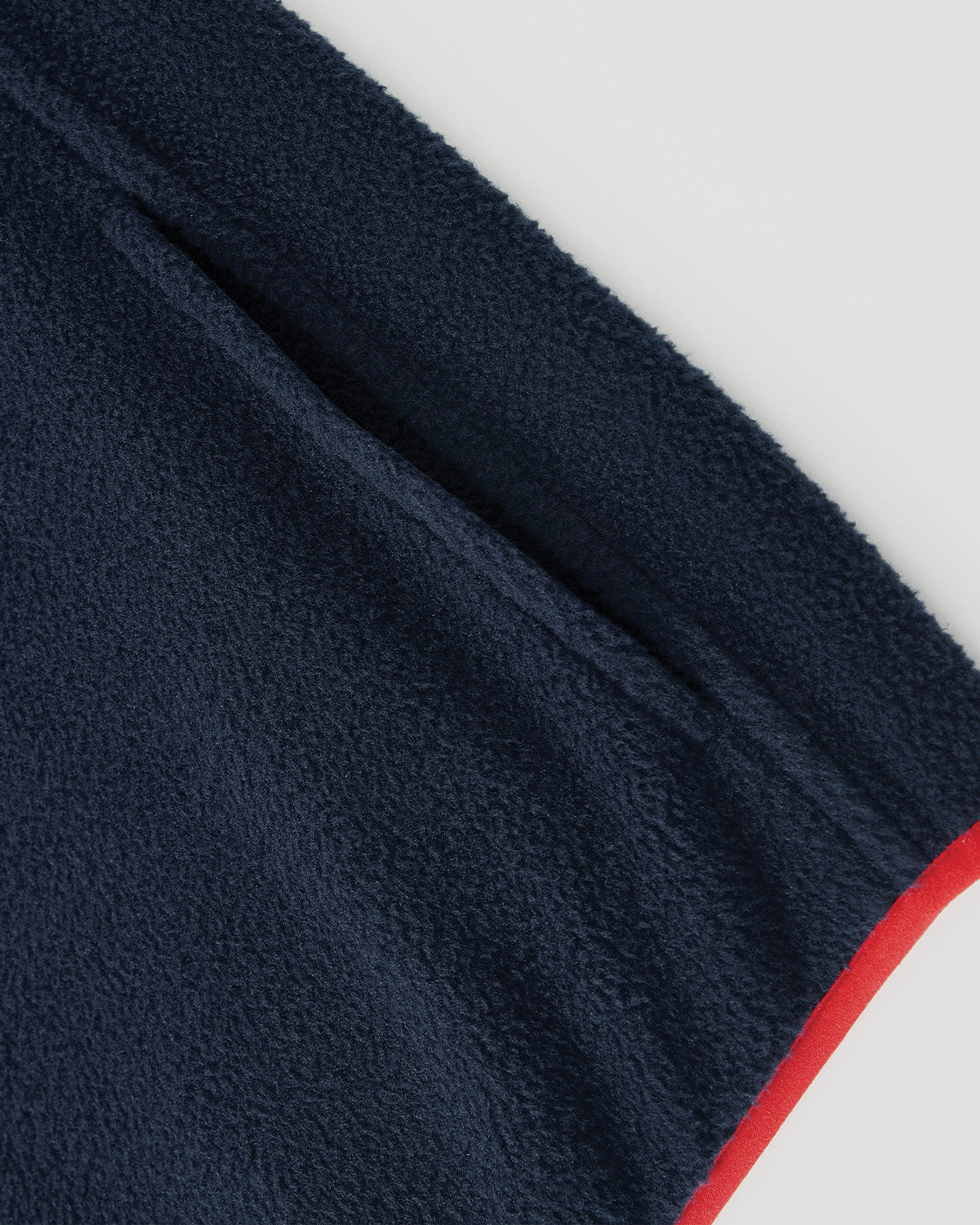 Close-up of the Sundae School NAVY TEARDROP KNOT FLEECE, showcasing its navy blue fabric, visible pocket, and red edge trim against a plain white background.