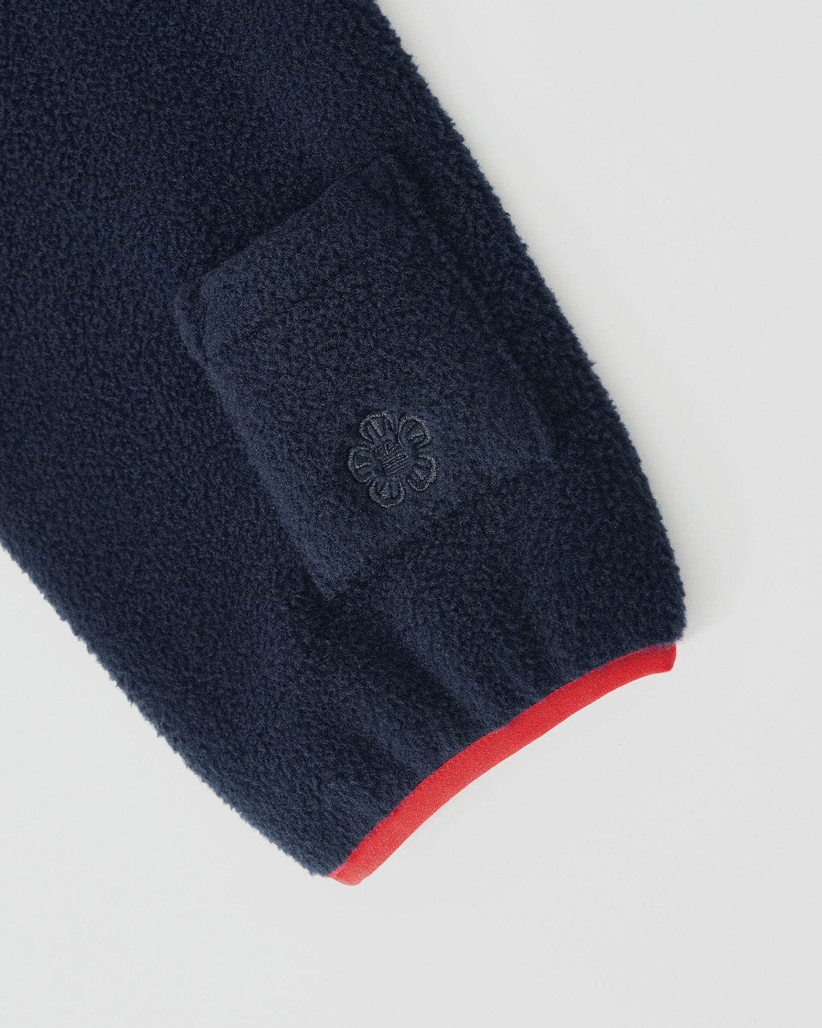 Close-up of Sundae School's NAVY TEARDROP KNOT FLEECE sleeve featuring a small square pocket, embroidered flower, and red-trimmed cuff.