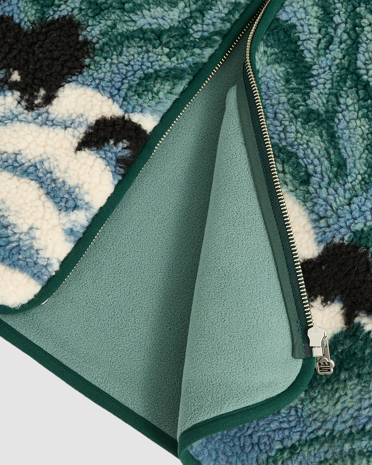 Close-up of the Sundae School TEAL FIVE PEAKS FLEECE jacket in teal and green, featuring a silver zipper, embossed pile fleece outer, smooth lining, and white, black, and blue shape patches.