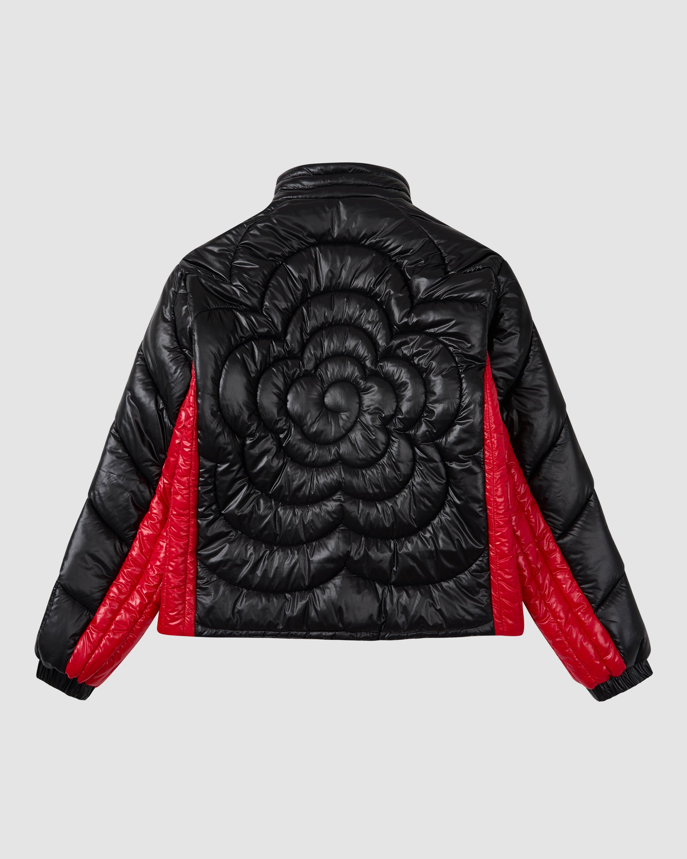 The BLACK RED MOCHI SPIRAL PUFFER by Sundae School features a black and red two-tone nylon shell, large quilted flower design on the back, and bold red sleeve and side panels, shown on a light gray background.