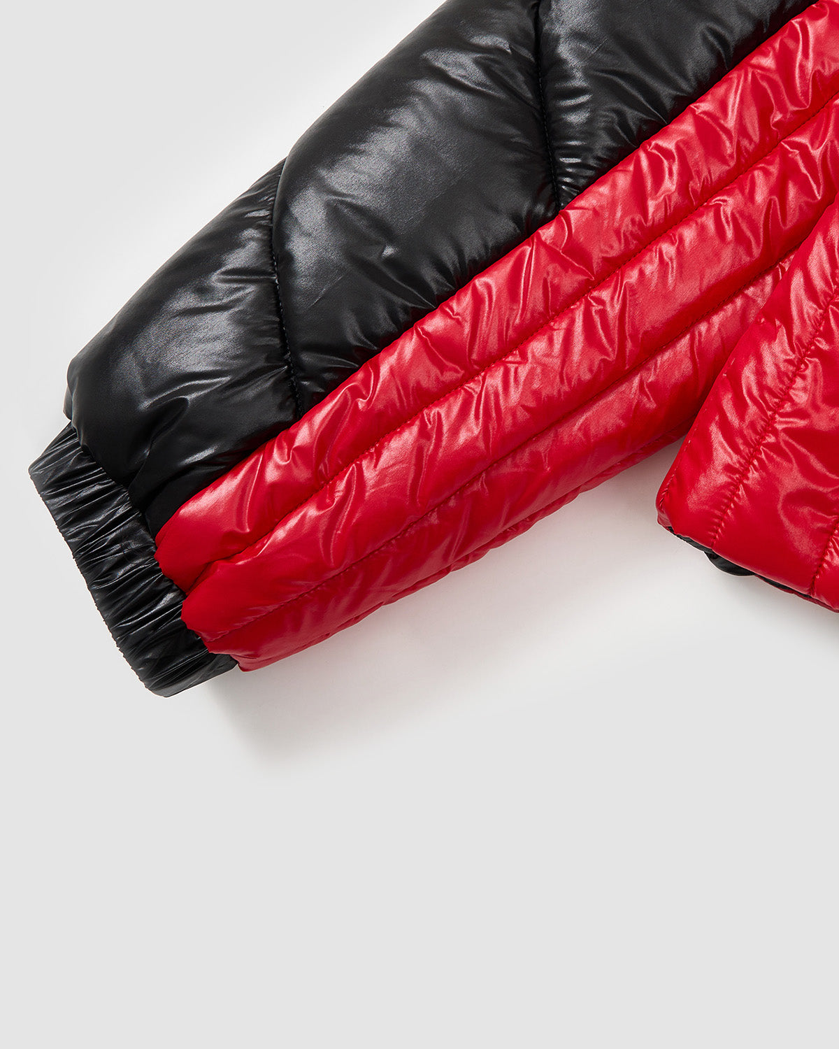 Close-up of the BLACK RED MOCHI SPIRAL PUFFER by Sundae School, featuring a shiny two-tone nylon shell sleeve in black and red with padding, visible stitching, an elastic cuff, and a modern biker-inspired style.