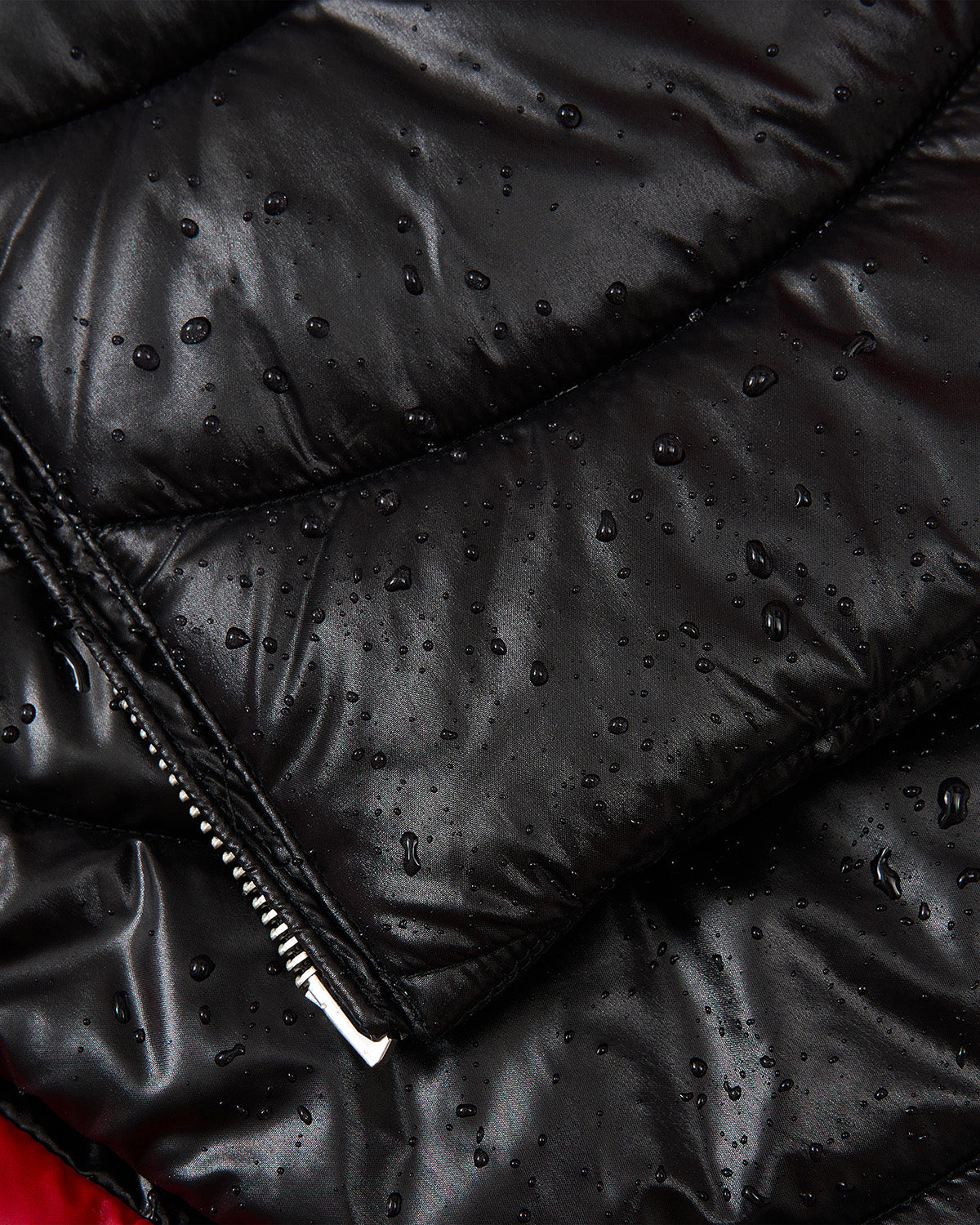 Close-up of Sundae School's BLACK RED MOCHI SPIRAL PUFFER, a black biker-inspired jacket with custom mochi spiral quilting, visible water droplets, a partial zipper, and red fabric in the background highlighting its unique style.