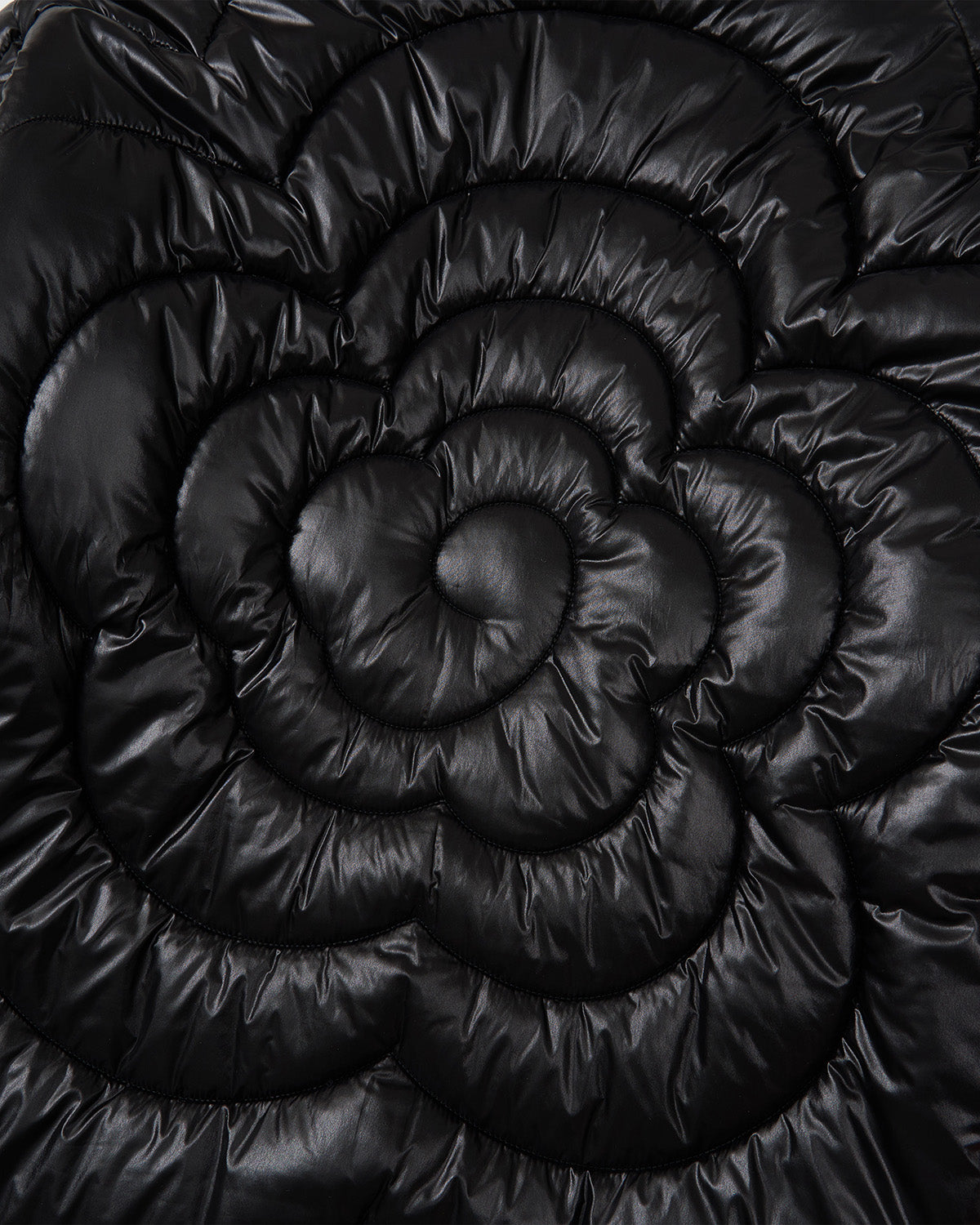 Close-up of Sundae School's BLACK RED MOCHI SPIRAL PUFFER, featuring shiny black quilted fabric with spiral flower stitching for a textured, puffy look—ideal for a biker-inspired jacket.