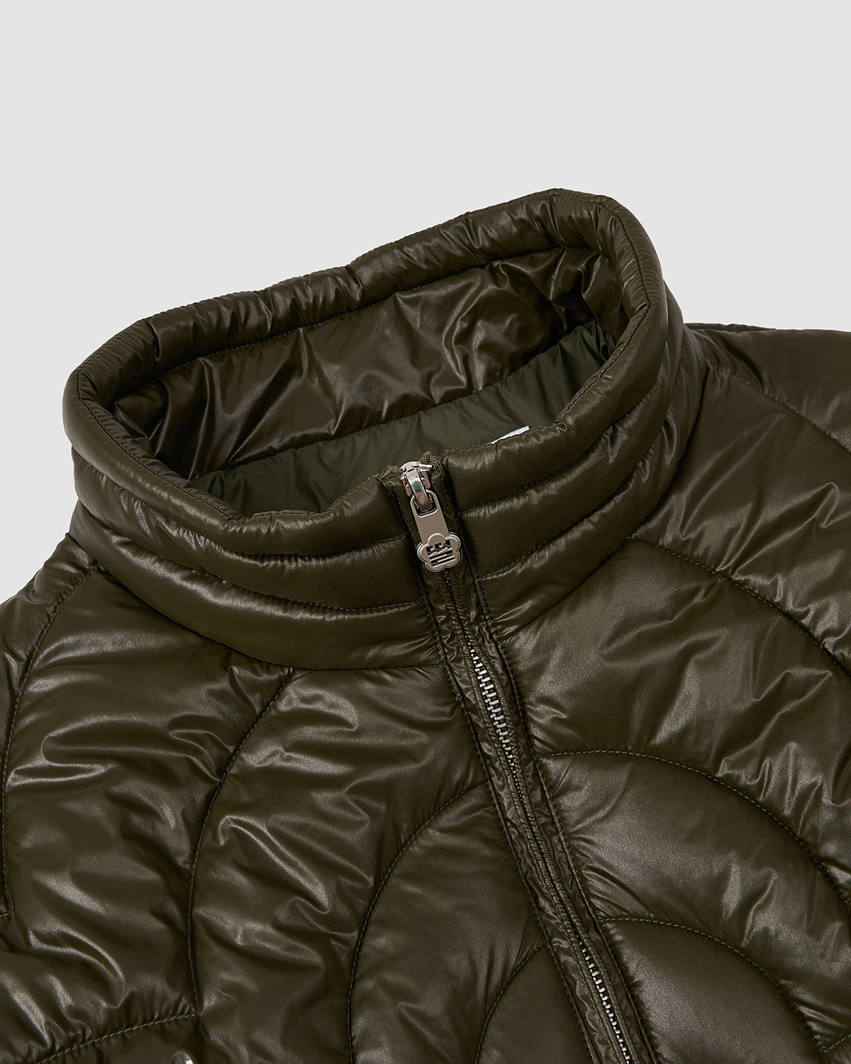 Close-up of the OLIVE OATMEAL MOCHI SPIRAL PUFFER by Sundae School—an olive green padded jacket with a high collar, shiny finish, visible front zipper, and stylish quilted circular pattern.