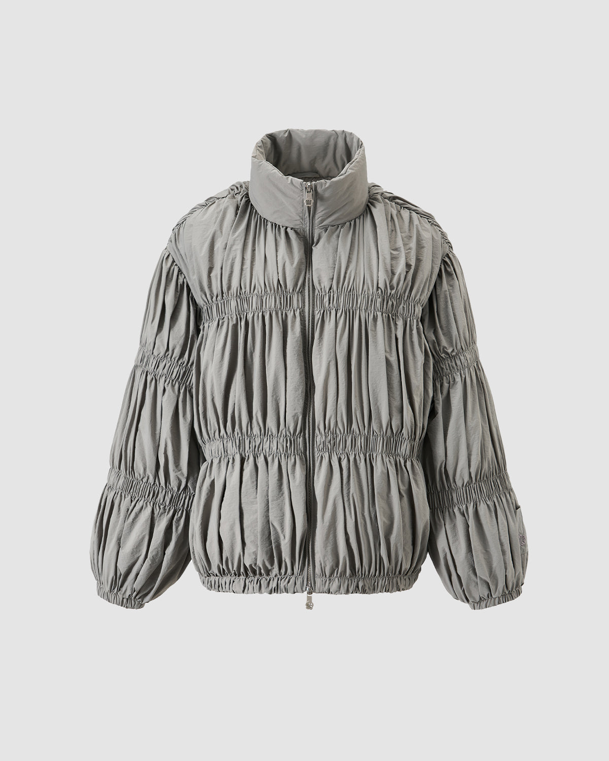 The Sundae School SMOKE PLEATED DUVET PUFFER is a light gray zip-up jacket with a high collar, all-over pleated ruching for texture and volume, long sleeves, and an elastic hem.