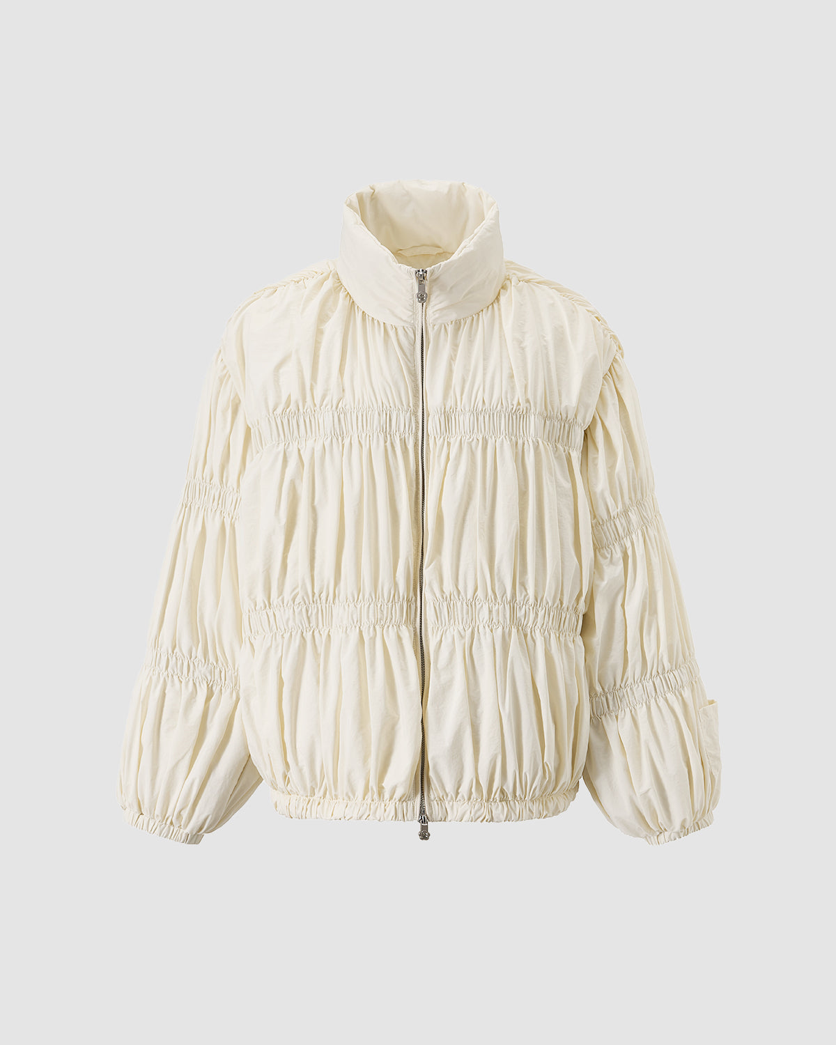 The IVORY PLEATED DUVET PUFFER by Sundae School is a cream-colored, long-sleeve duck down jacket featuring a stand collar, ruched details, elasticated cuffs and hem, and a front zipper, shown on a light gray background.