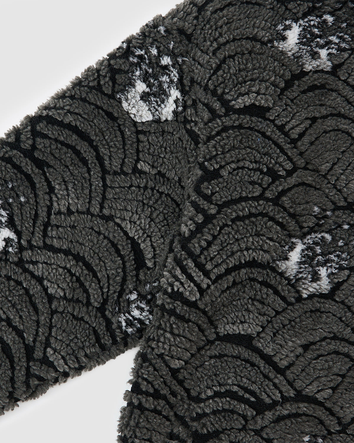 A close-up of Sundae School’s BLACK WAVE FLEECE shows its distinctive jacquard design, featuring textured dark gray fabric with black scalloped wave patterns and subtle white patches.