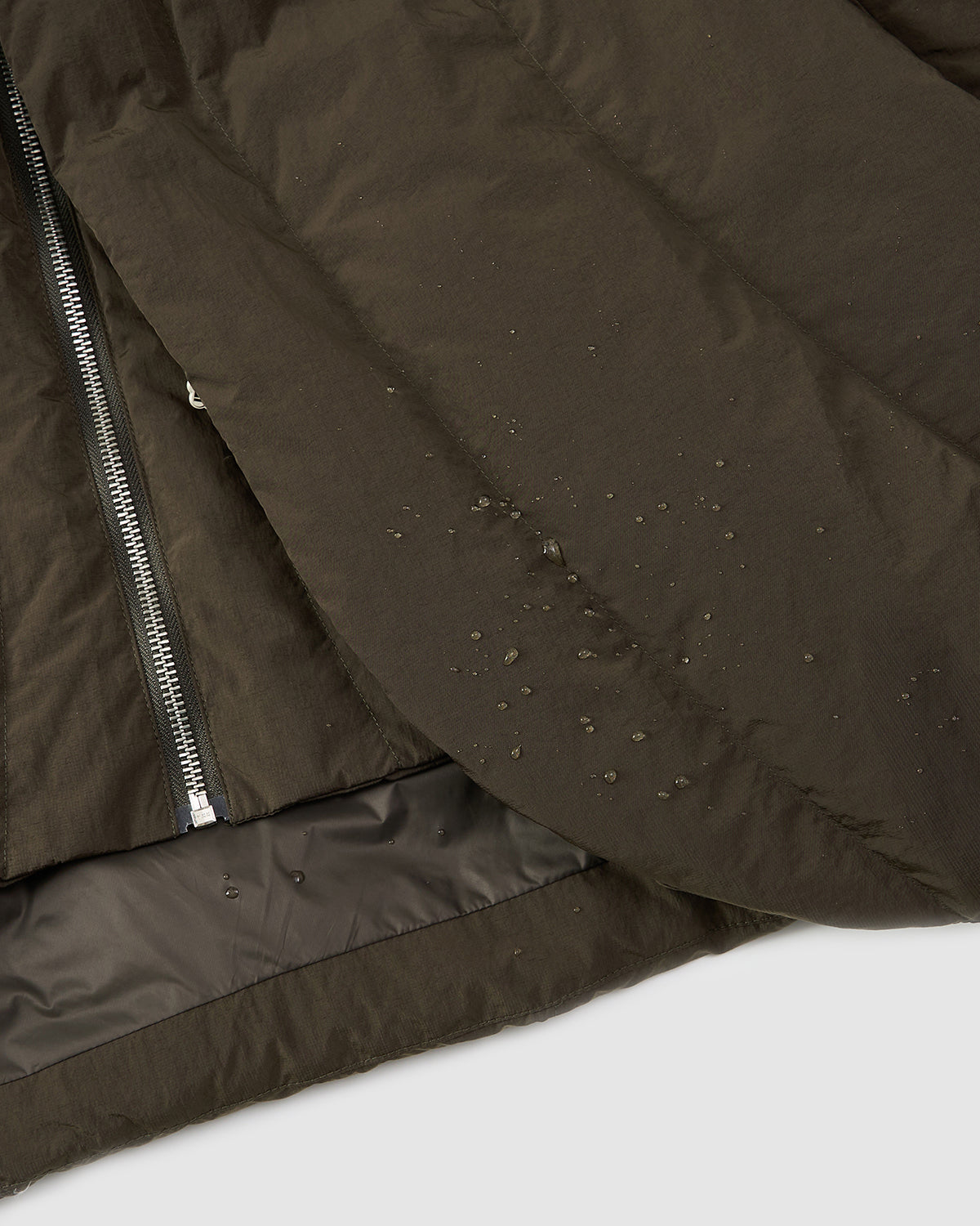A close-up of Sundae School's [PRE-ORDER] KHAKI HEAVYWEIGHT MOCHI PUFFER shows its hanbok-inspired design, visible zipper, and water-resistant fabric with droplets beading on the dark olive-green material.
