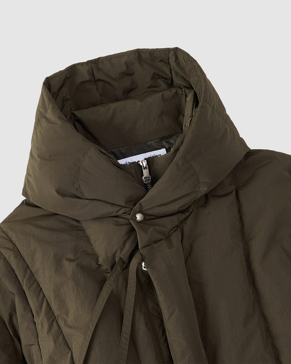 A close-up of the Sundae School [PRE-ORDER] KHAKI HEAVYWEIGHT MOCHI PUFFER, a hanbok-inspired jacket with a high padded collar, mochi quilting, zip closure, and snap buttons, shown on a light gray background.