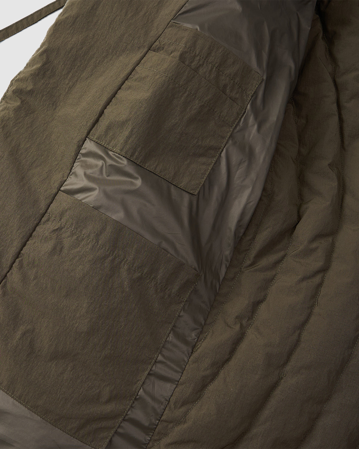 Close-up of Sundae School’s [PRE-ORDER] KHAKI HEAVYWEIGHT MOCHI PUFFER, a hanbok-inspired jacket with a large rectangular patch pocket and shiny quilted panels stitched onto a textured background.