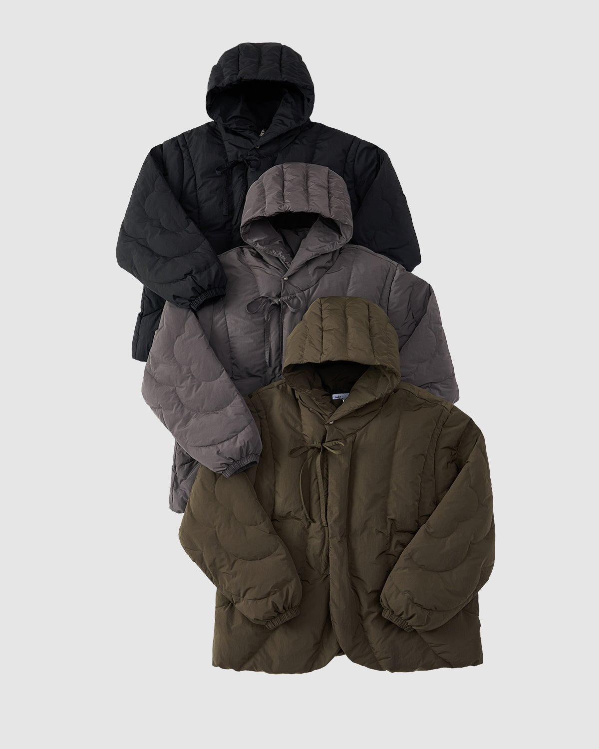 Three CHARCOAL HEAVYWEIGHT MOCHI PUFFER jackets by Sundae School in black, dark gray, and olive green are vertically arranged on a light gray background, each featuring quilted stitching and stylish front tie closures.