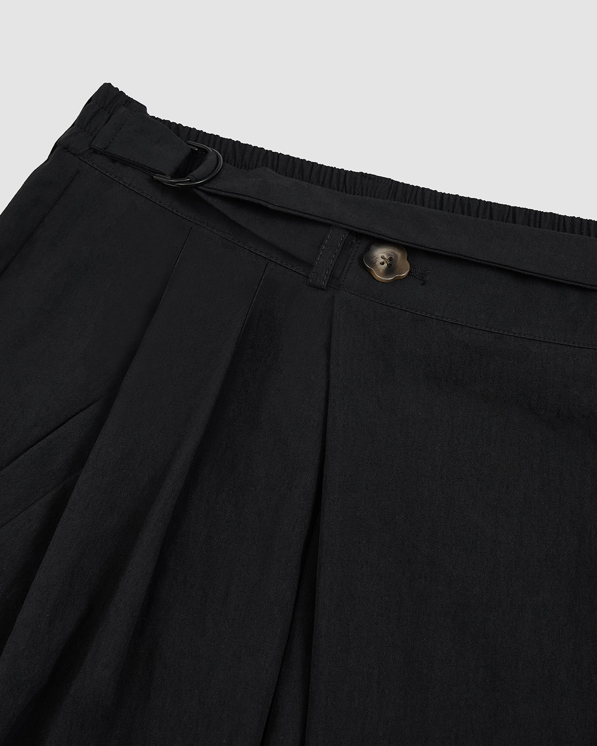 Close-up of black elastic waistband with D-ring belt attachment and front pleating detail on Sundae School nylon pants