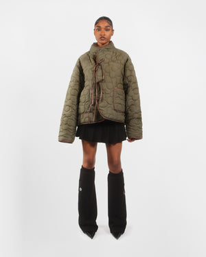 Female model wearing the olive green quilted side of the Reversible Flower Quilted Jeogori Fleece with brown tie closures visible, over a black mini skirt.