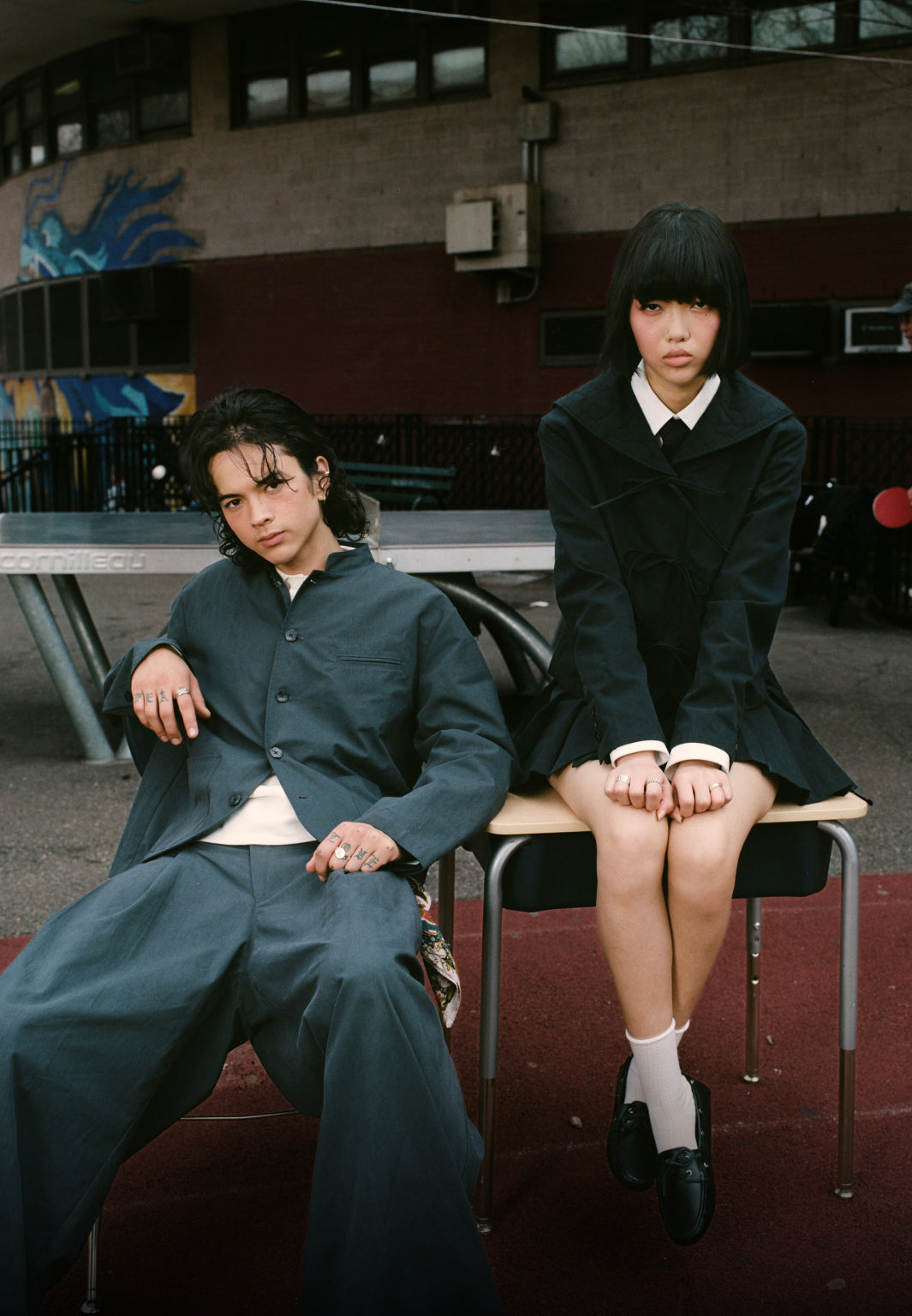 Two people sitting on chairs in a schoolyard with other students in the background wearing Sundae School Stand Collar Uniform Jacket and Pleated Uniform Slacks, Sailor Collar Uniform Jacket, and Uniform Apron Skirt 