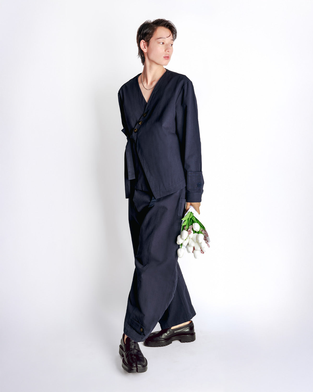 Three-quarters view of model wearing the Hanbok Balloon Pants holding white flowers, showing the wide-leg silhouette and relaxed fit.