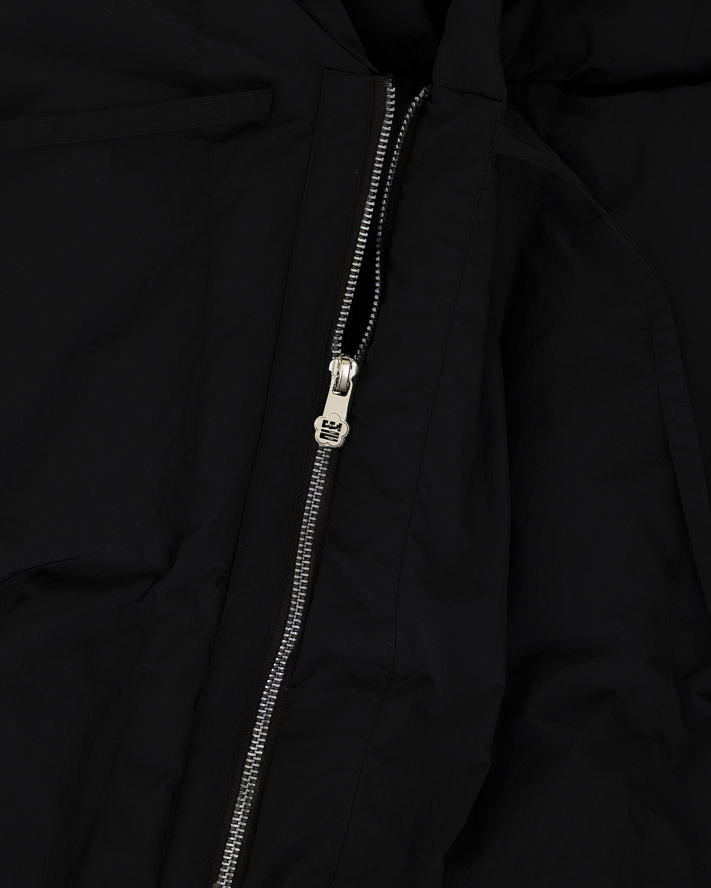 Close-up of a silver zipper partially unzipped on black fabric, featuring the Sundae School [PRE-ORDER] BLACK HEAVYWEIGHT MOCHI PUFFER. The zipper pull is centered and highlights the jacket’s premium details.